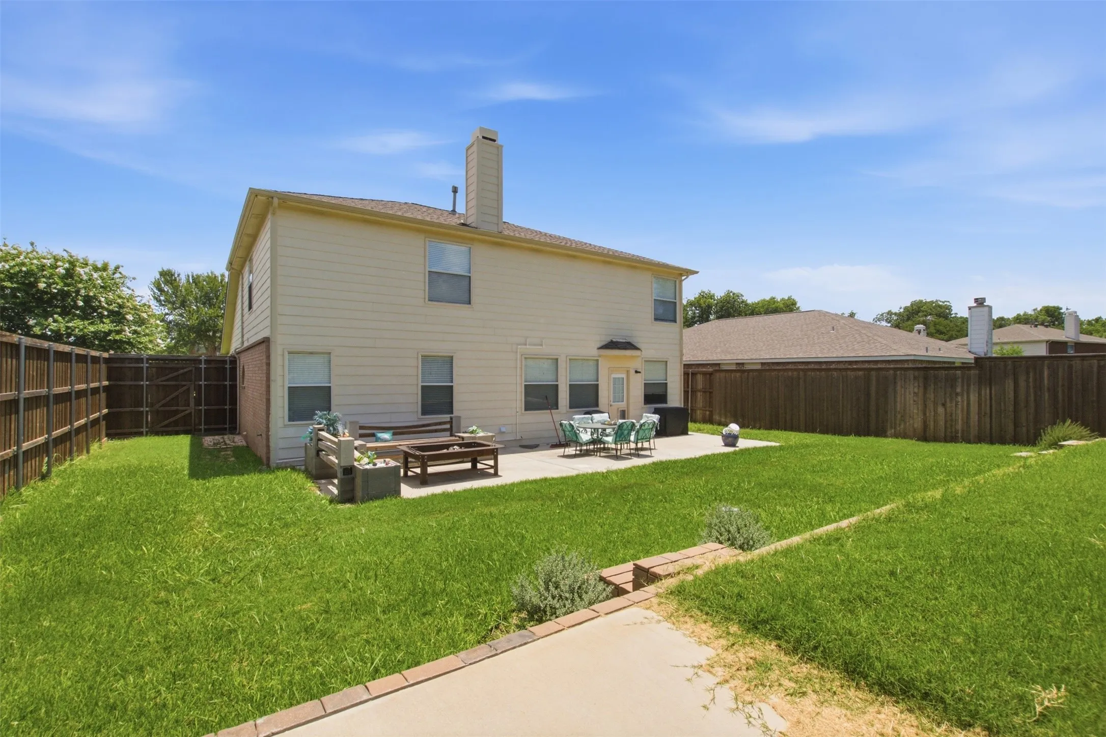 Expansive backyard featuring a two-story residence with light-colored siding, a patio area, a fenced perimeter, and a level lawn