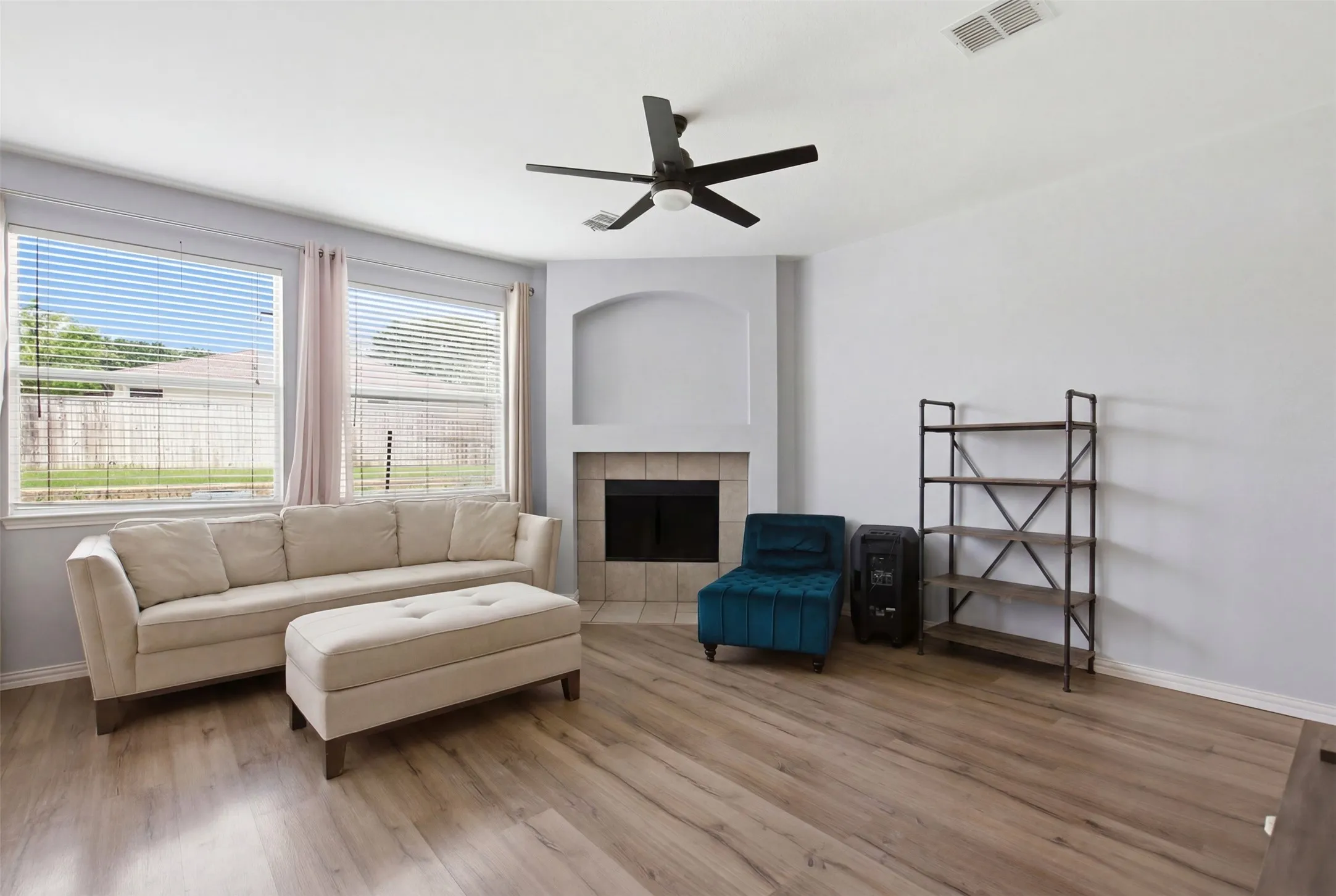 Living area featuring wood-finish flooring, a corner fireplace with a tiled surround, an arched alcove, and a ceiling fan
