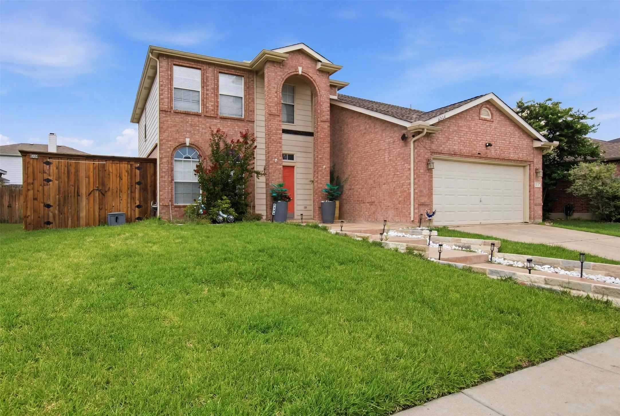 Brick facade residence featuring an arched entryway, two-car garage, and a wood privacy fence