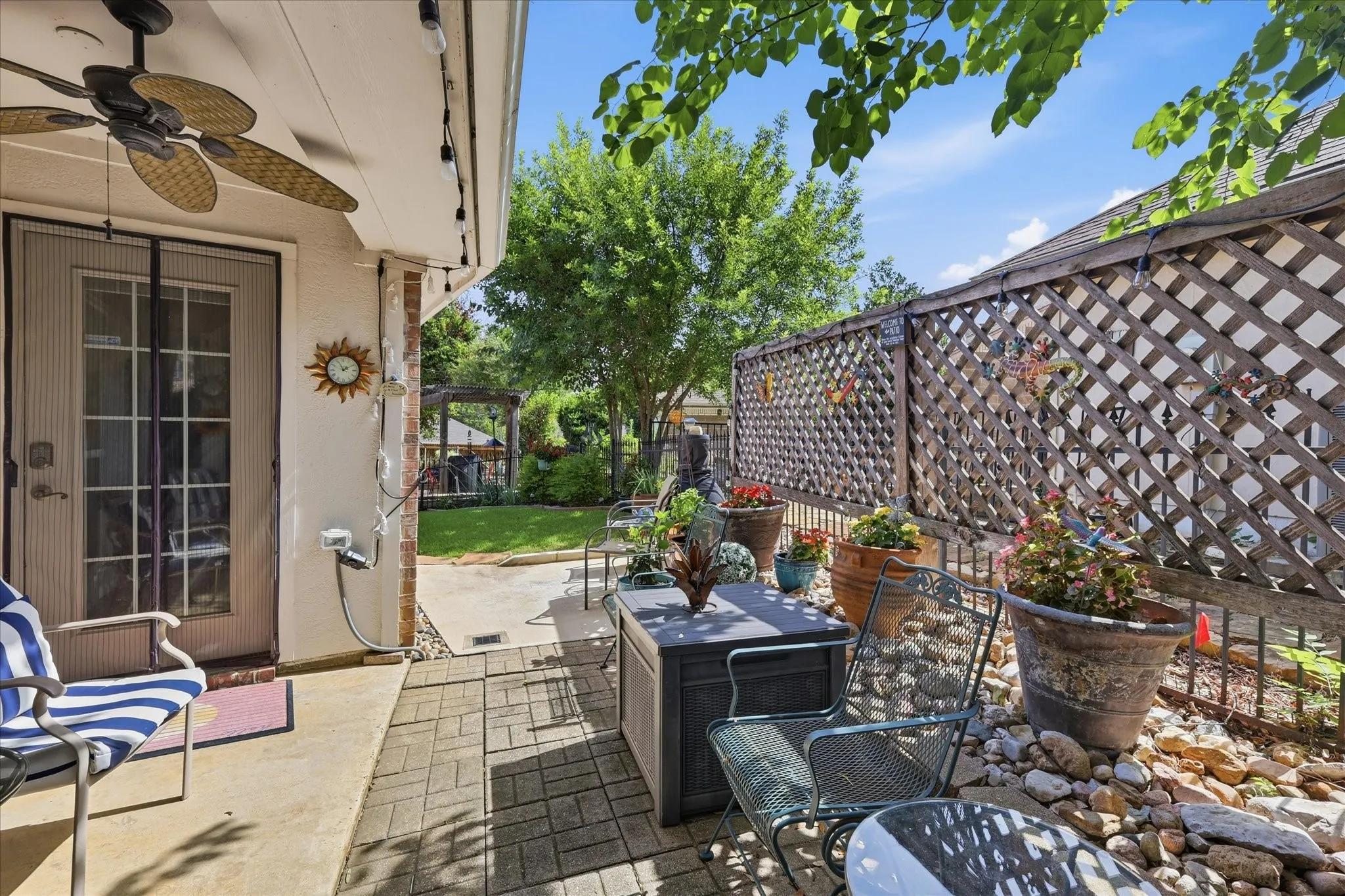 Covered patio area featuring a glass-paned door, a ceiling fan, string lighting, and brick accents