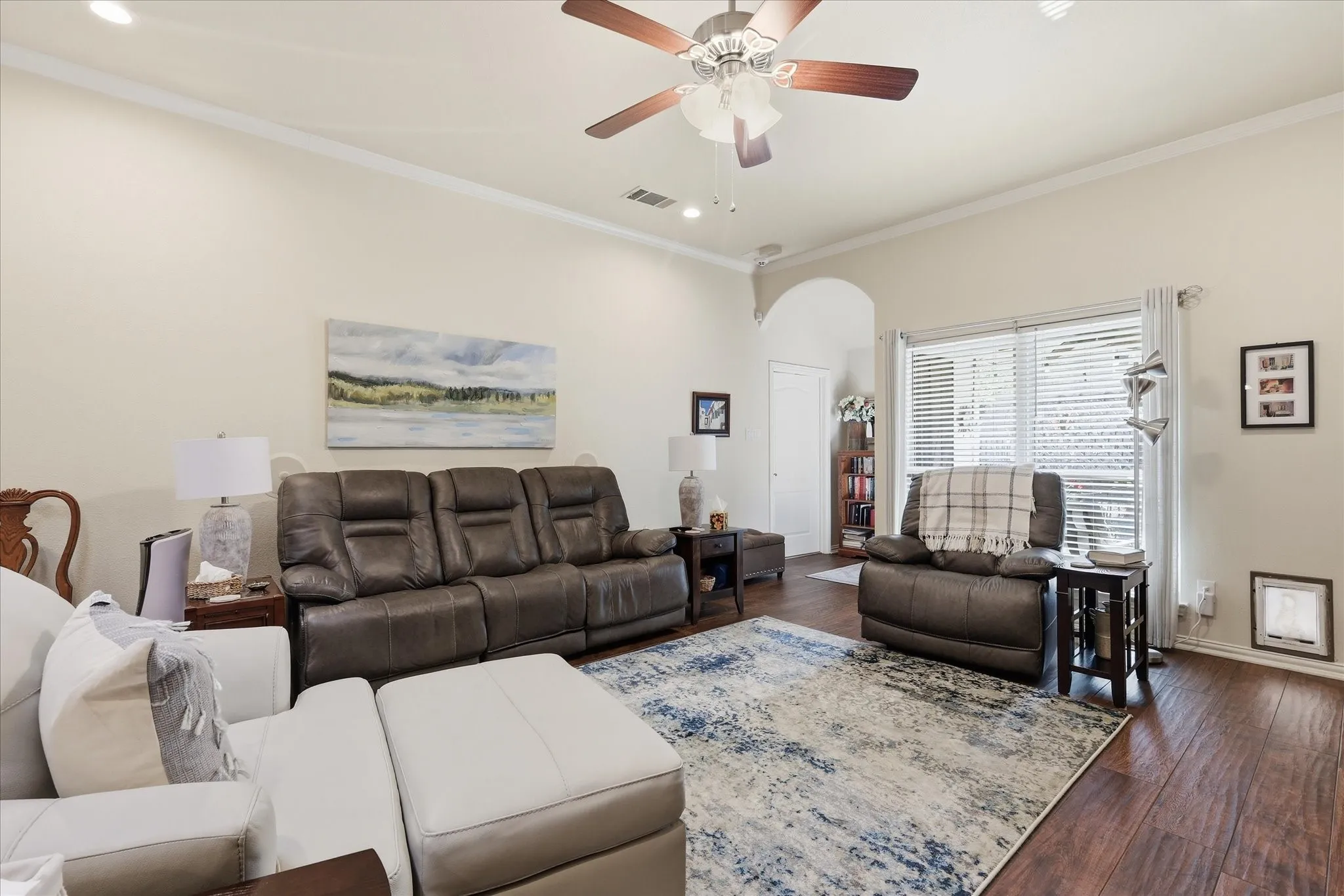 Spacious living area featuring wood-finish flooring, vaulted ceilings with crown molding, and a ceiling fan with integrated lighting