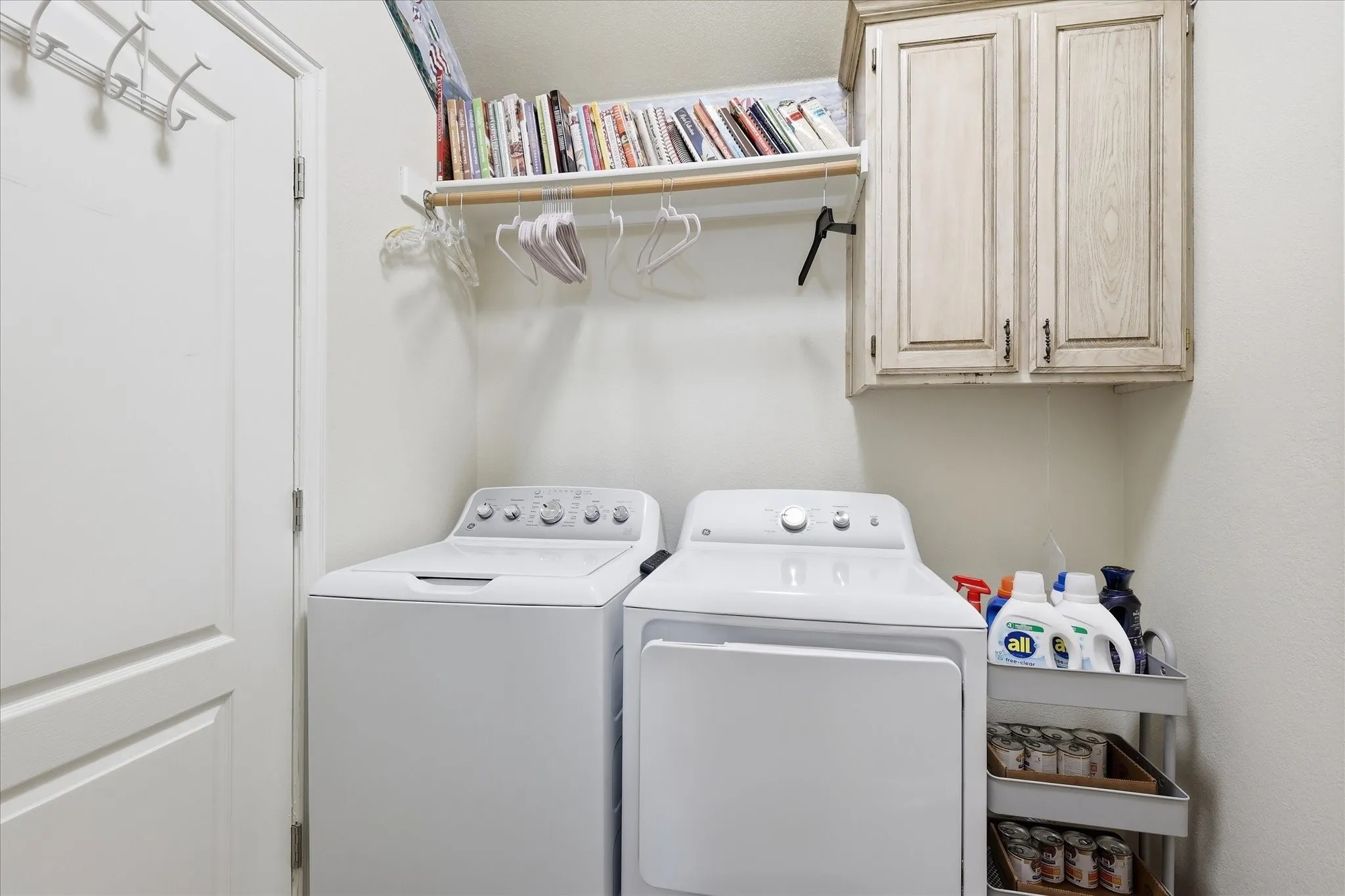 Dedicated utility area featuring overhead cabinetry, wall-mounted shelving, and a hanging rod