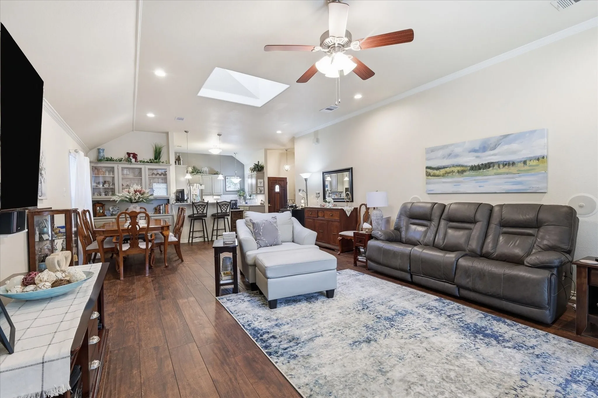 Open concept living area featuring wood-finish flooring, a skylight, and a ceiling fan