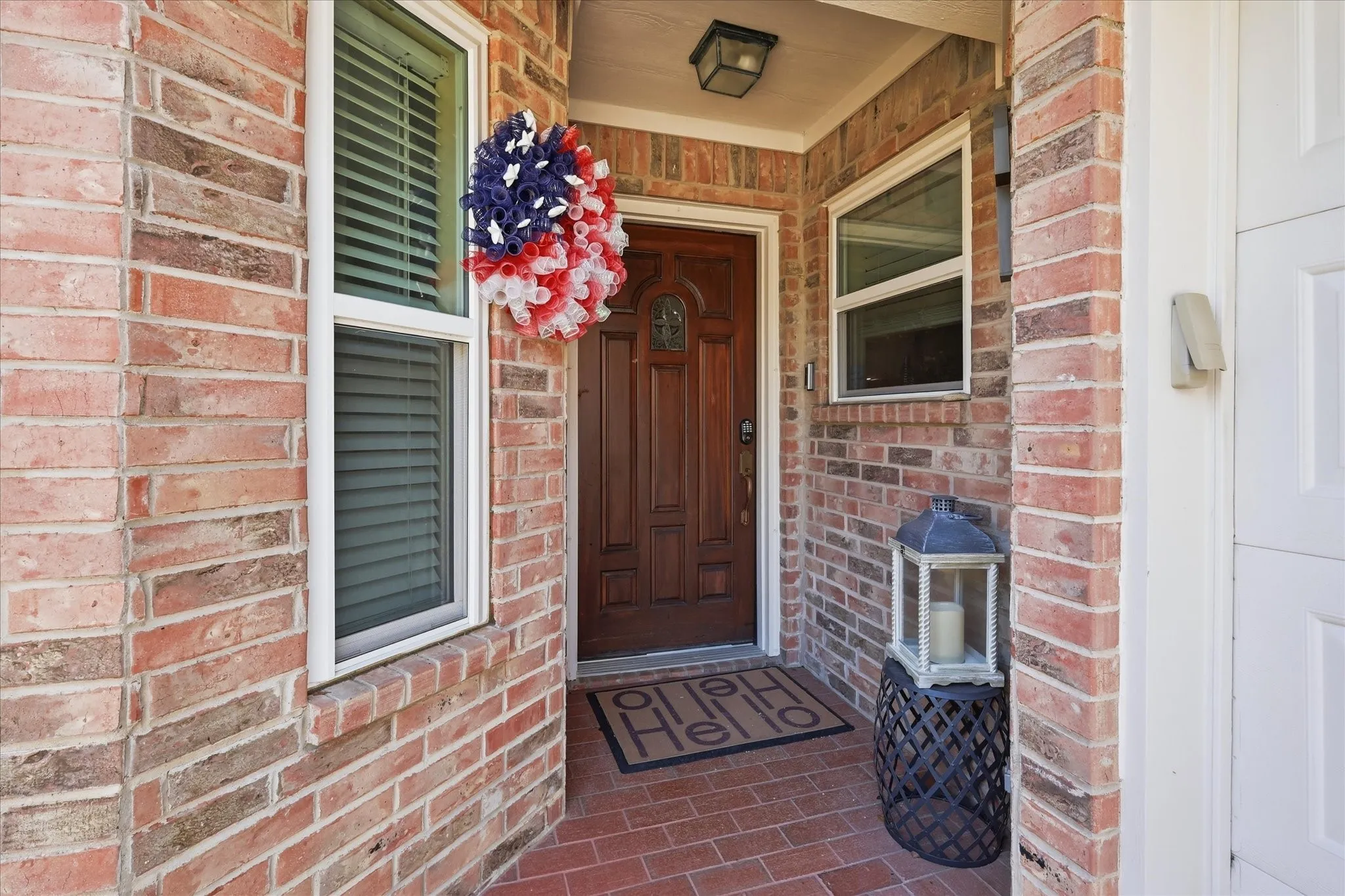 Inviting brick exterior featuring a recessed entry, a paneled wood-finish front door, white-framed windows with blinds, and a brick-finish porch