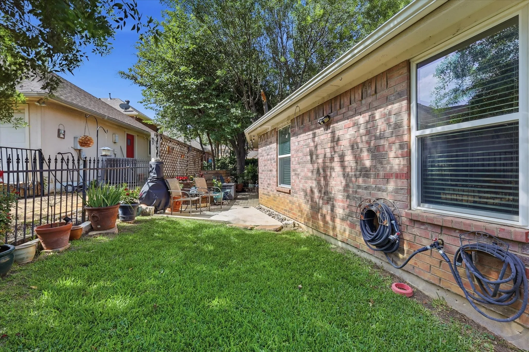 Manicured lawn with a brick exterior, framed by mature trees, and featuring a paved patio area