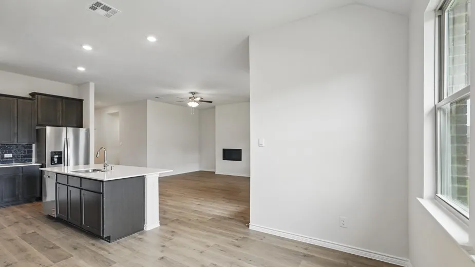 Open-concept living area featuring wood-finish flooring, a contemporary kitchen island with a built-in sink, stainless steel appliances, dark cabinetry, and recessed lighting