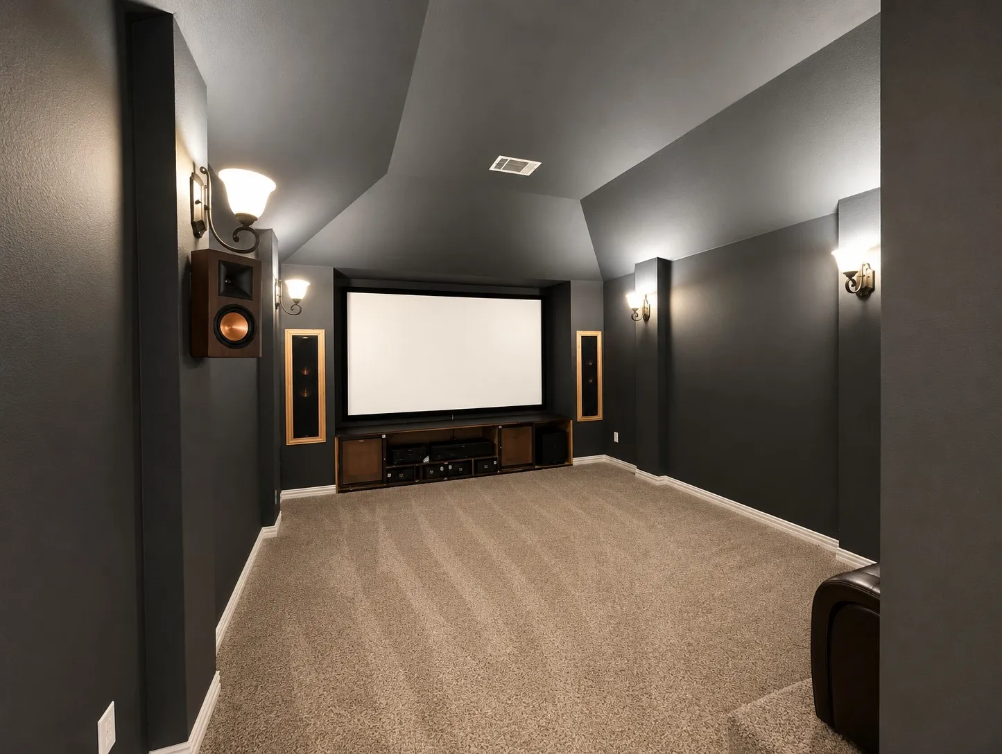 Dedicated media room featuring a large projector screen, dark accent walls, angled ceilings, and wall-mounted sconce lighting