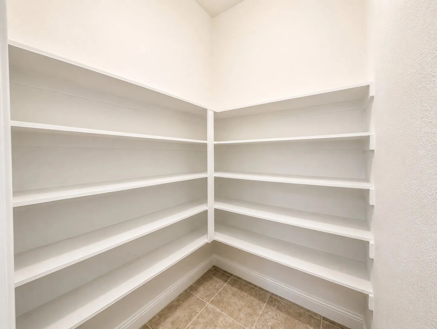 Spacious pantry featuring multiple tiers of built-in shelving, tile flooring, and light-toned walls