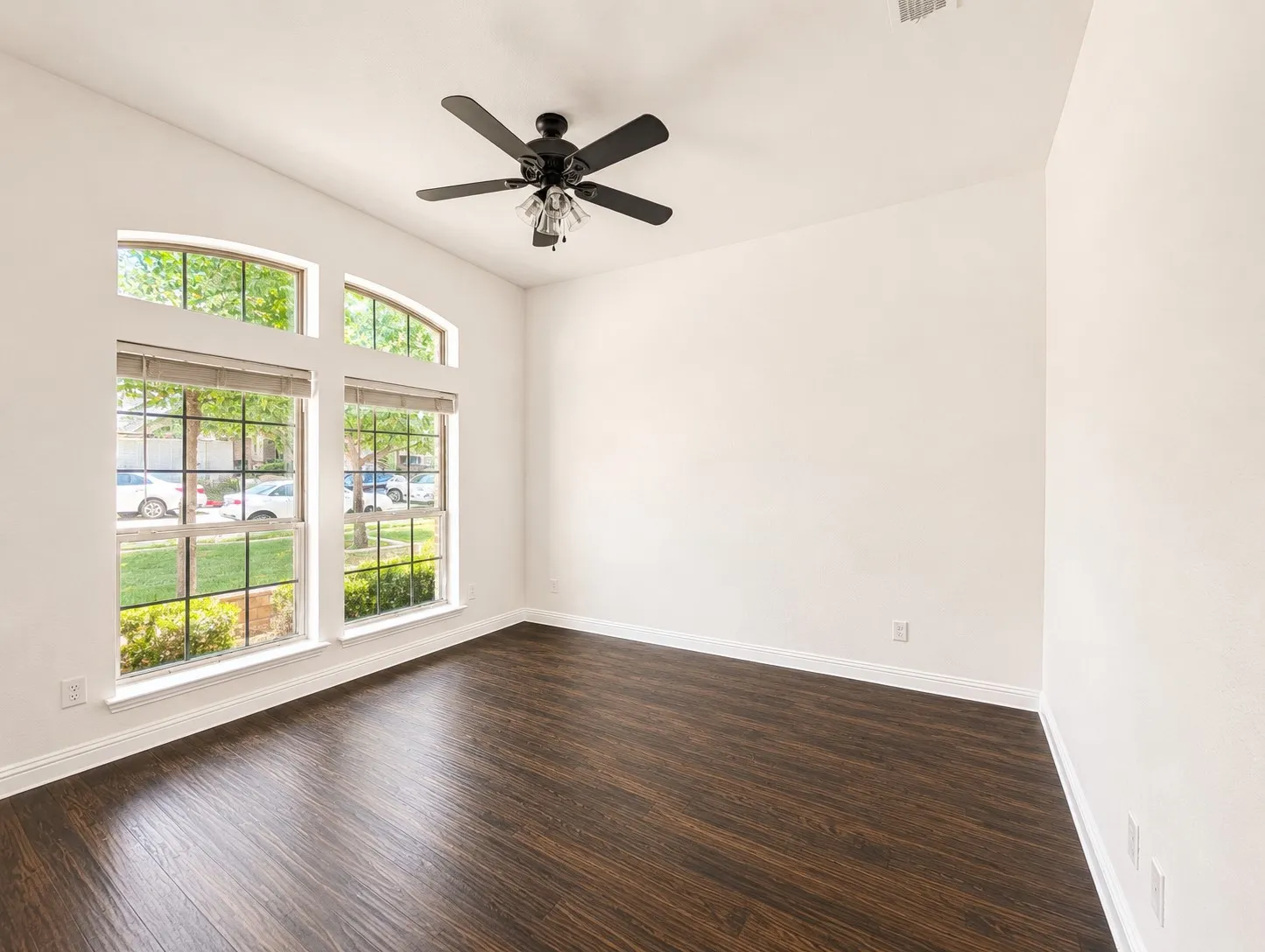 Room featuring expansive arched windows, dark wood-finish flooring, a vaulted ceiling, a ceiling fan with integrated lighting, and white baseboards