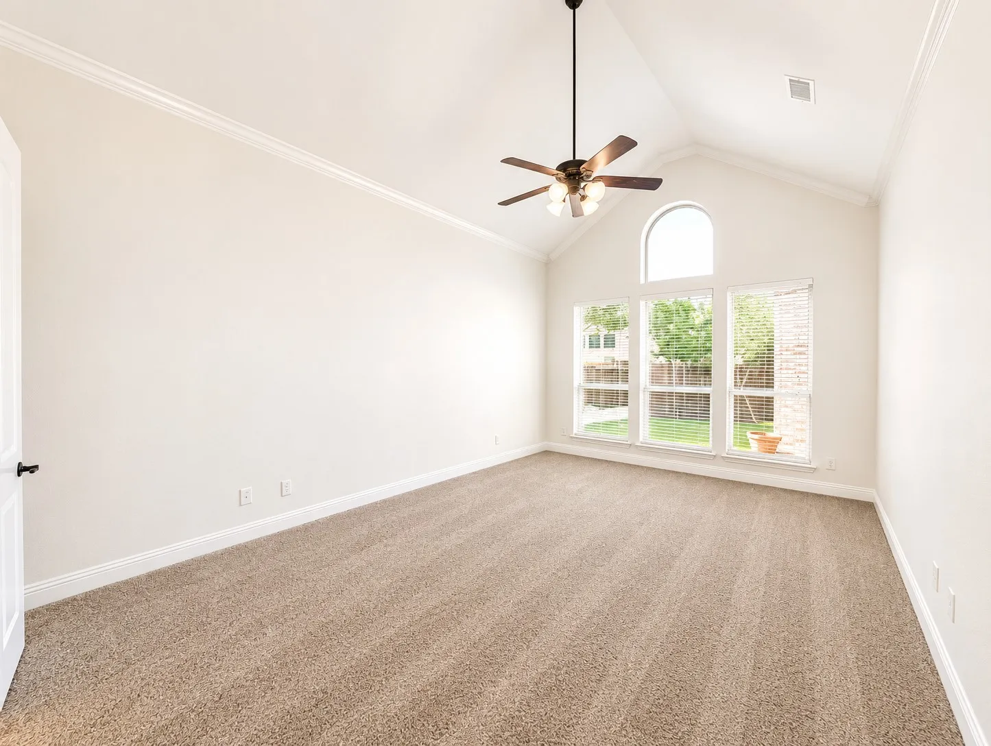 Room featuring a vaulted ceiling with crown molding, three large windows, an arched transom window, and a ceiling fan with light fixture