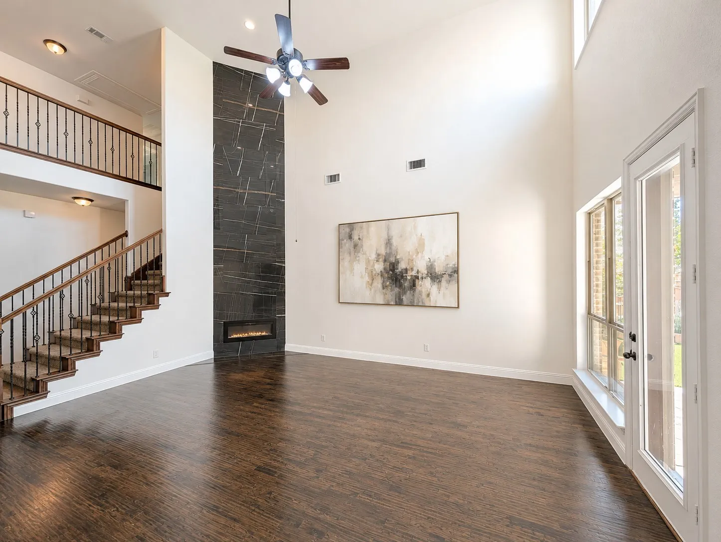 Two-story living area featuring dark wood-finish flooring, a contemporary fireplace with a dark stone-look surround, and a ceiling fan with integrated lighting