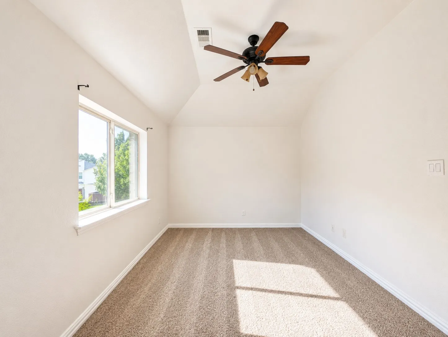 Spacious room featuring vaulted ceilings, a ceiling fan with integrated lighting, and neutral wall tones