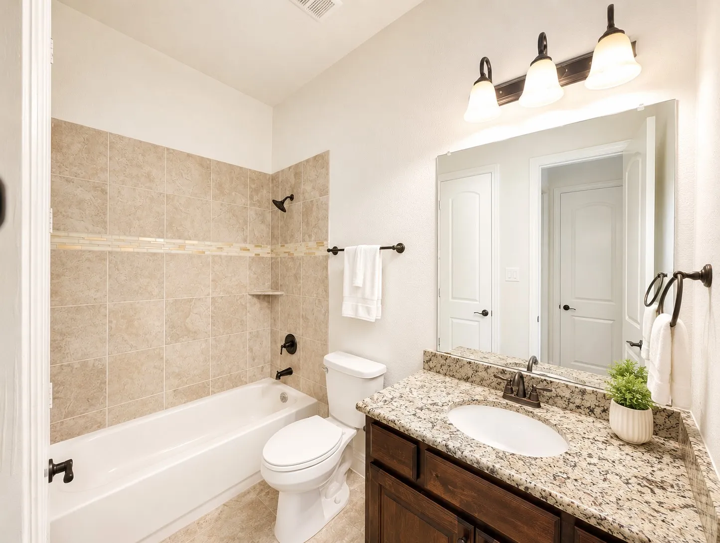 Full bathroom featuring a tub/shower combination with tiled surround and decorative accent band, a single vanity with granite-finish countertop, undermount sink, and dark wood-finish cabinetry, and oil-rubbed bronze fixtures