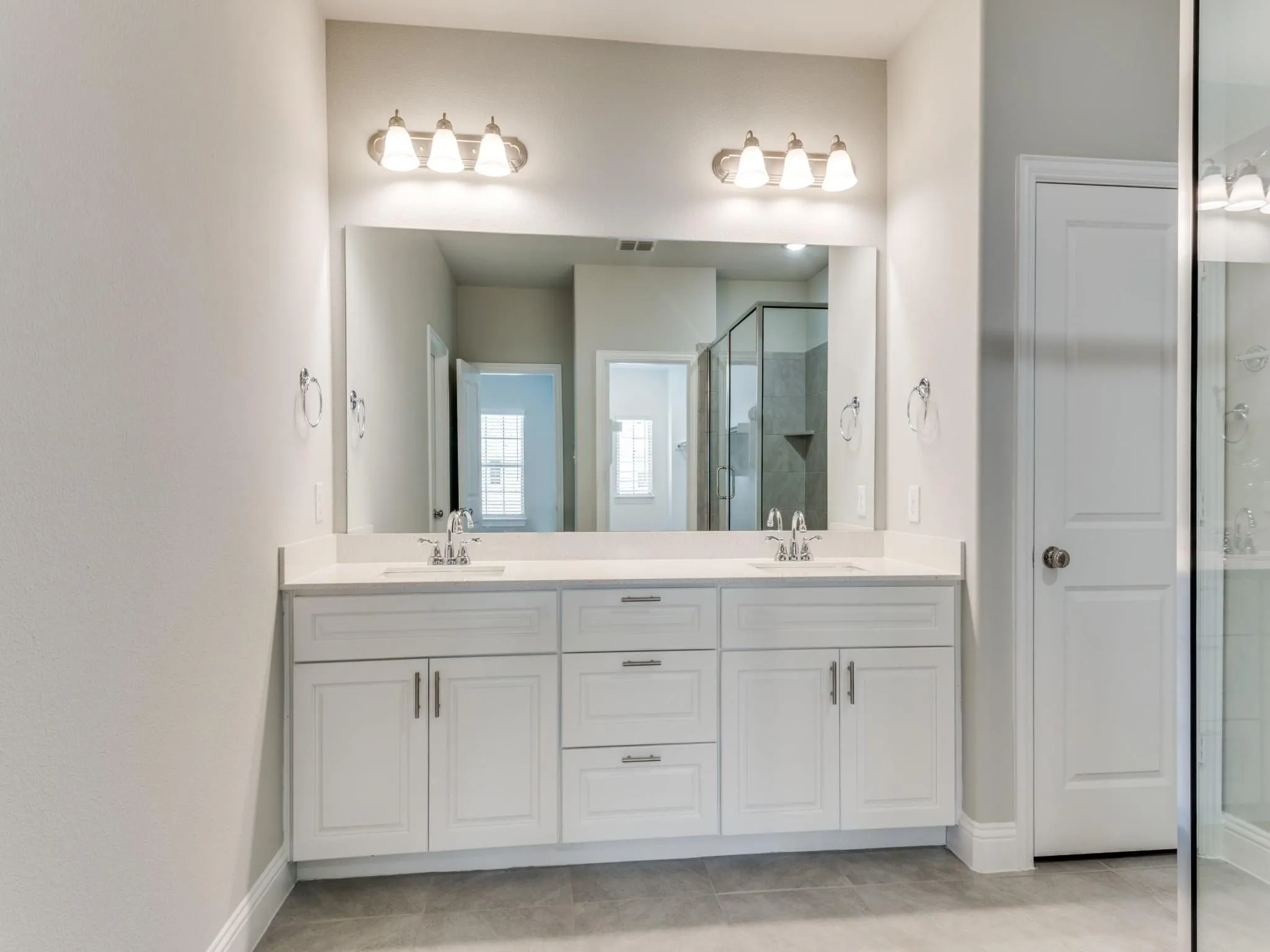 Dual white vanity with undermount sinks, chrome fixtures, and a large framed mirror with overhead lighting