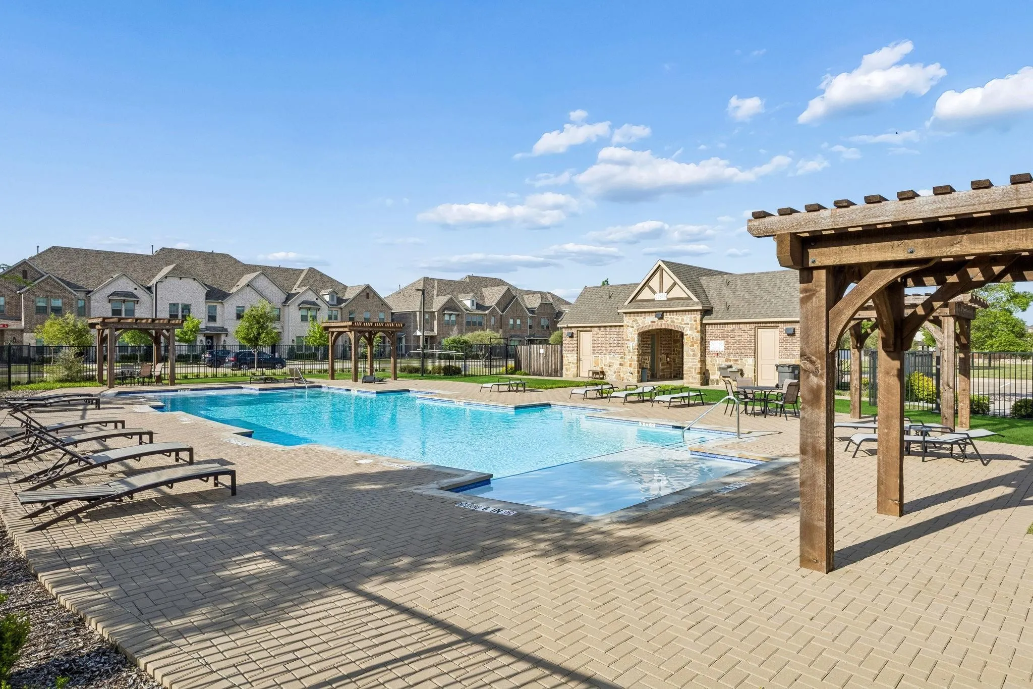 Resort-style swimming pool featuring a paver deck, multiple wooden pergolas, and an adjacent stone-clad building