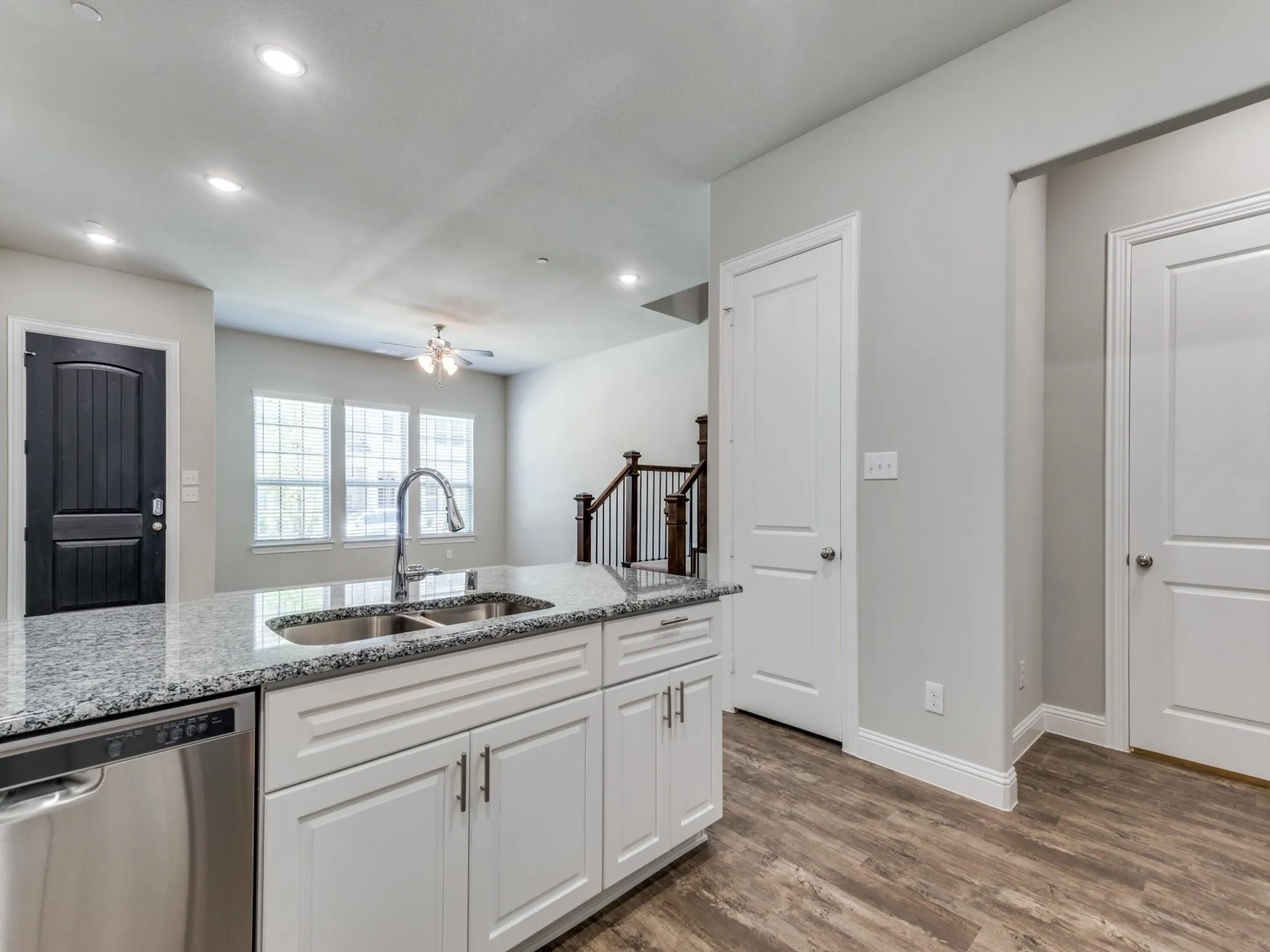 Kitchen island featuring a dual basin sink with a gooseneck faucet, light granite-finish countertop, white cabinetry with silver hardware, and an integrated stainless steel dishwasher