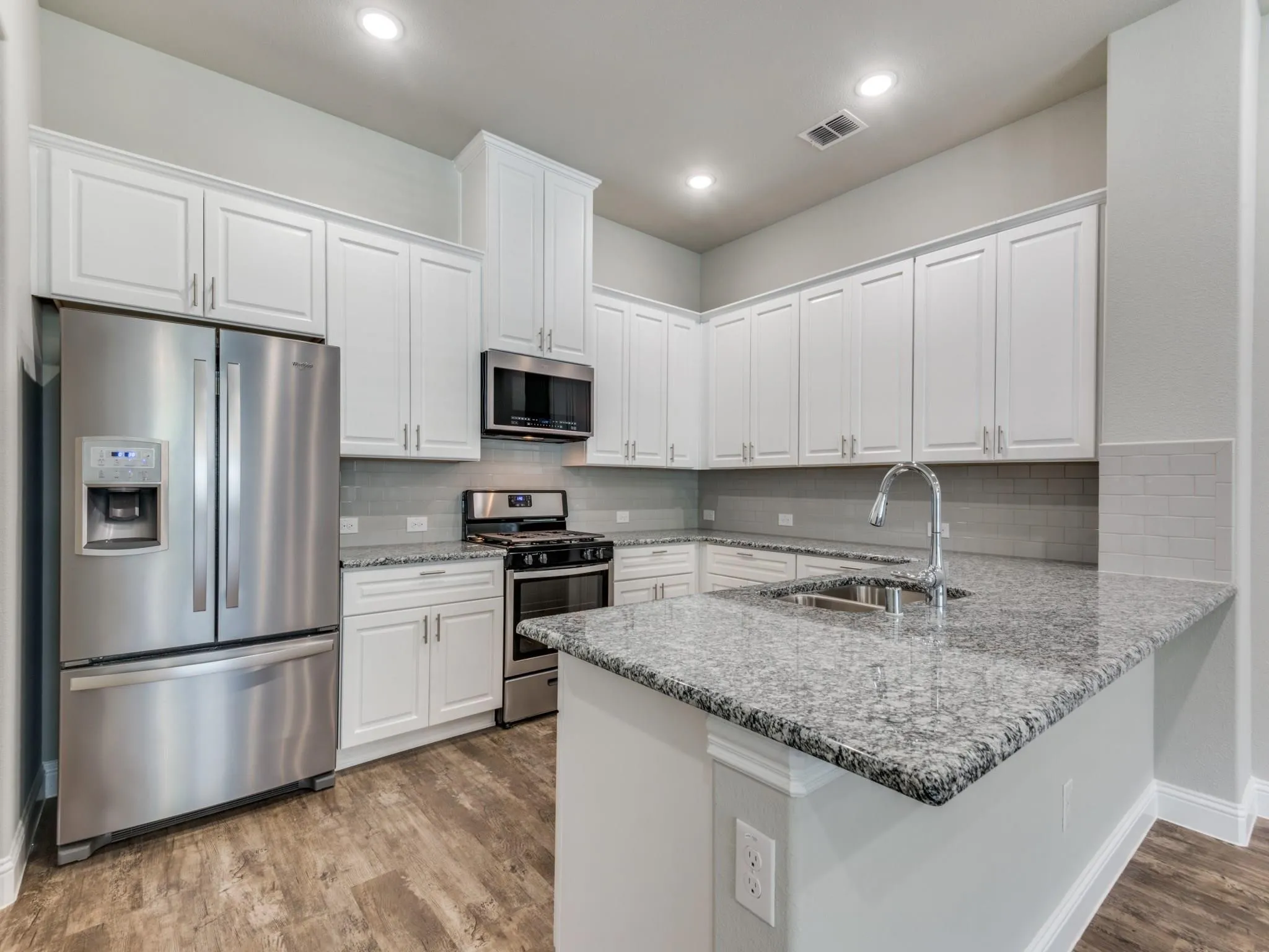 Modern kitchen featuring white shaker cabinetry, stainless steel appliances, speckled stone countertops, a subway tile backsplash, and wood-finish flooring