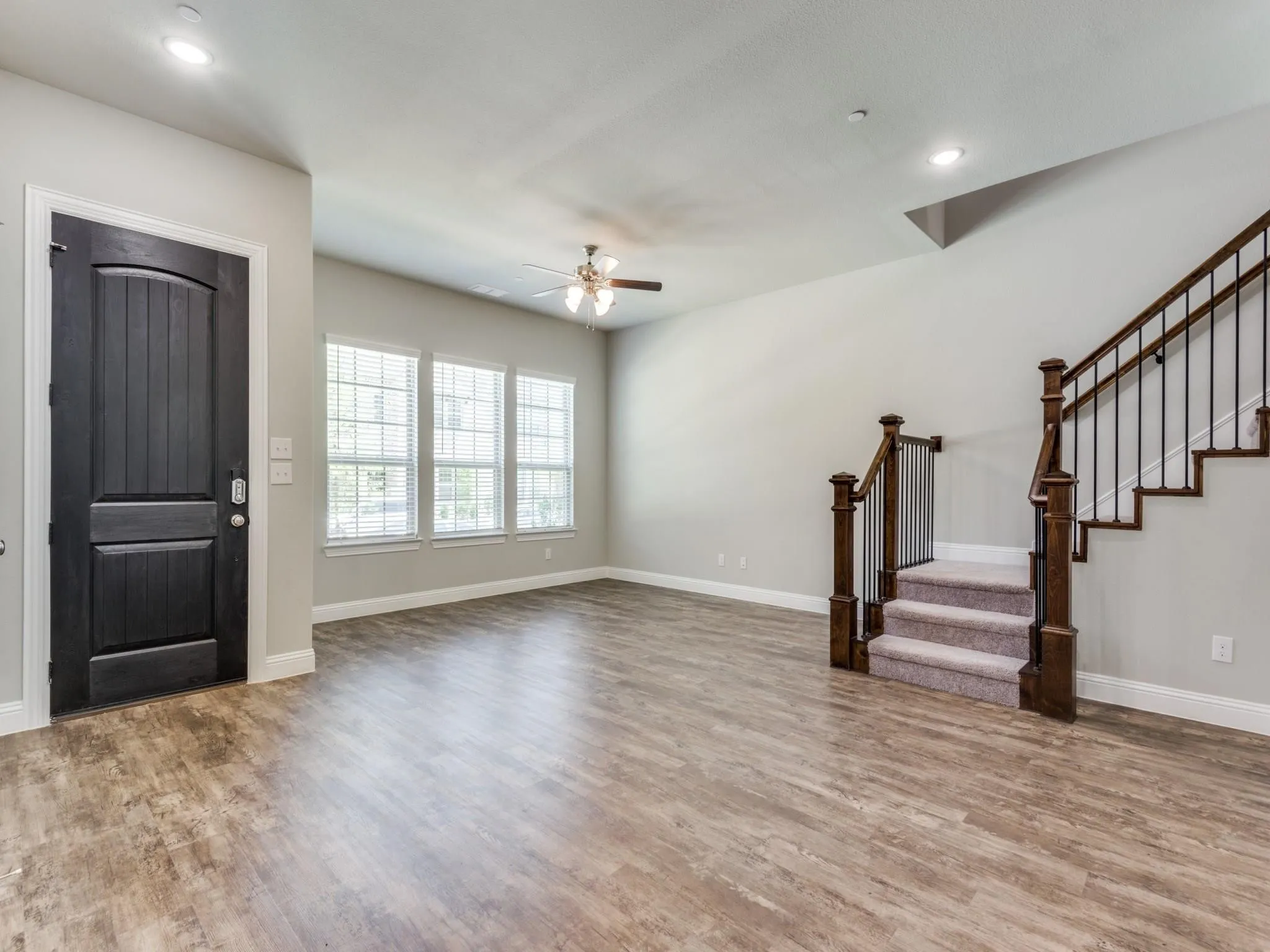 Spacious living area featuring wood-finish flooring, a dark wood staircase with wrought iron balusters, and a contemporary ceiling fan
