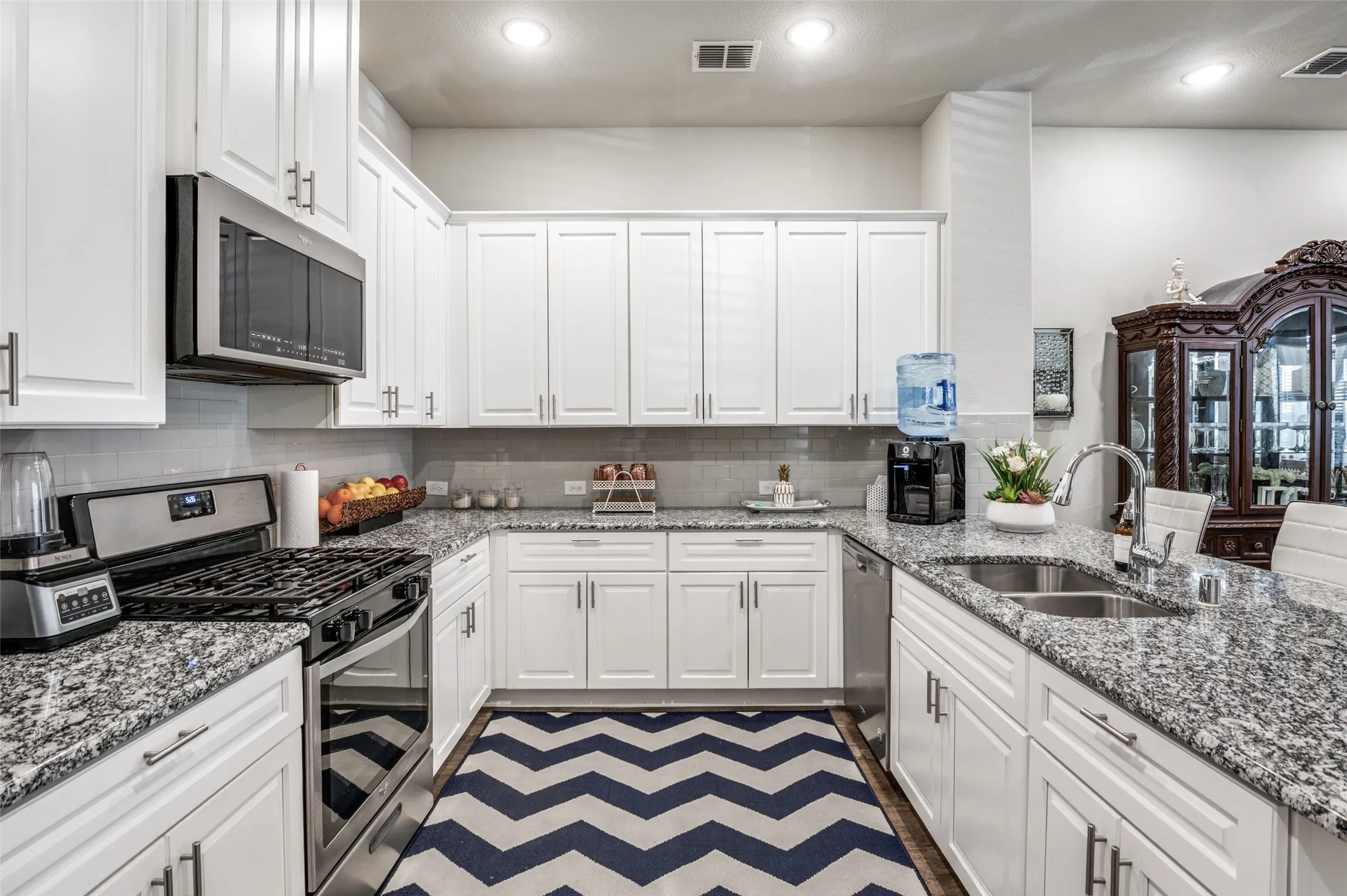 Modern kitchen featuring white cabinetry with brushed nickel hardware, speckled granite countertops, a built-in stainless steel microwave, and a stainless steel gas range