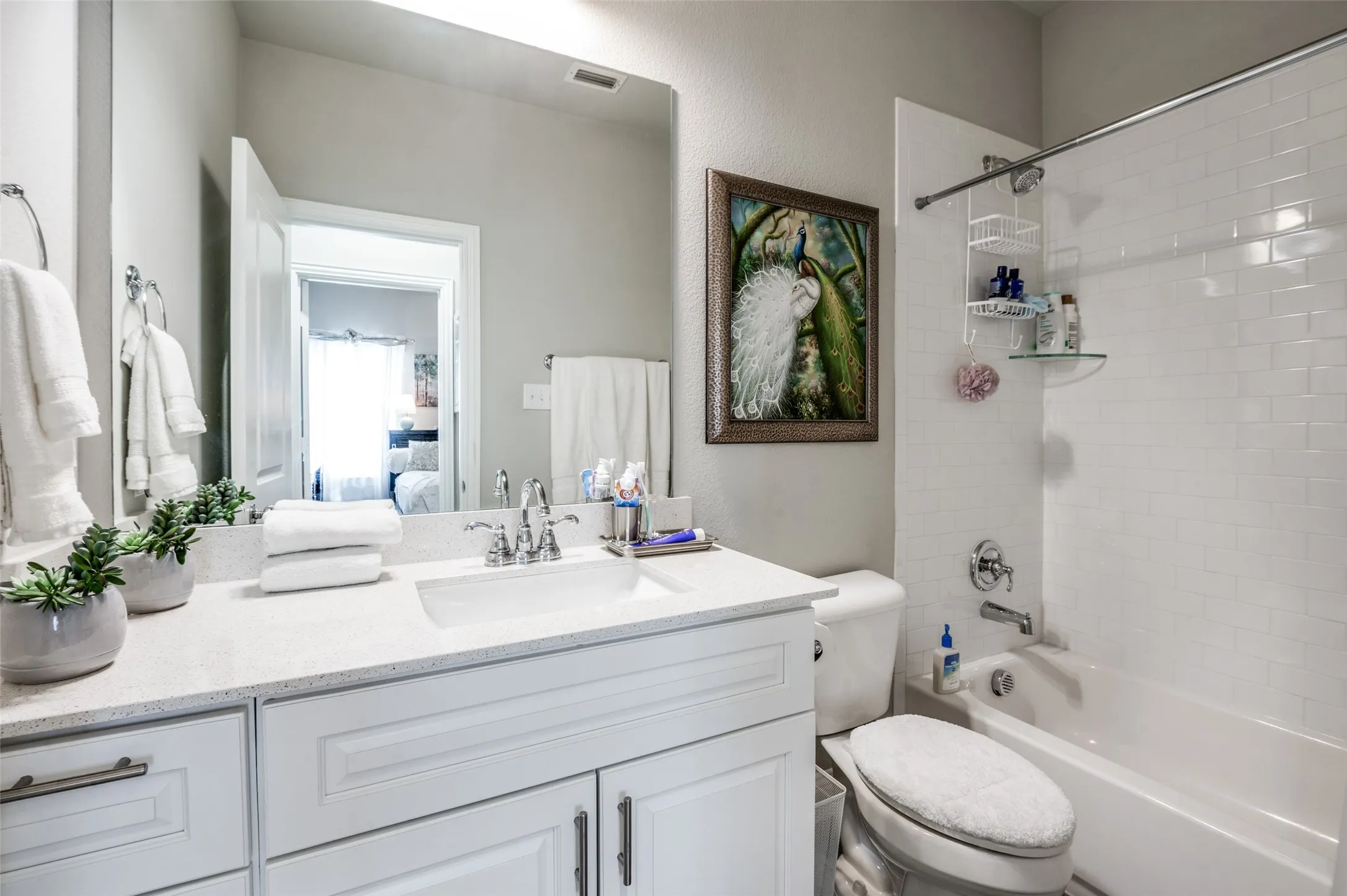 Bathroom featuring a white subway tile shower surround, a white vanity with shaker-style cabinetry, and a light-colored speckled countertop