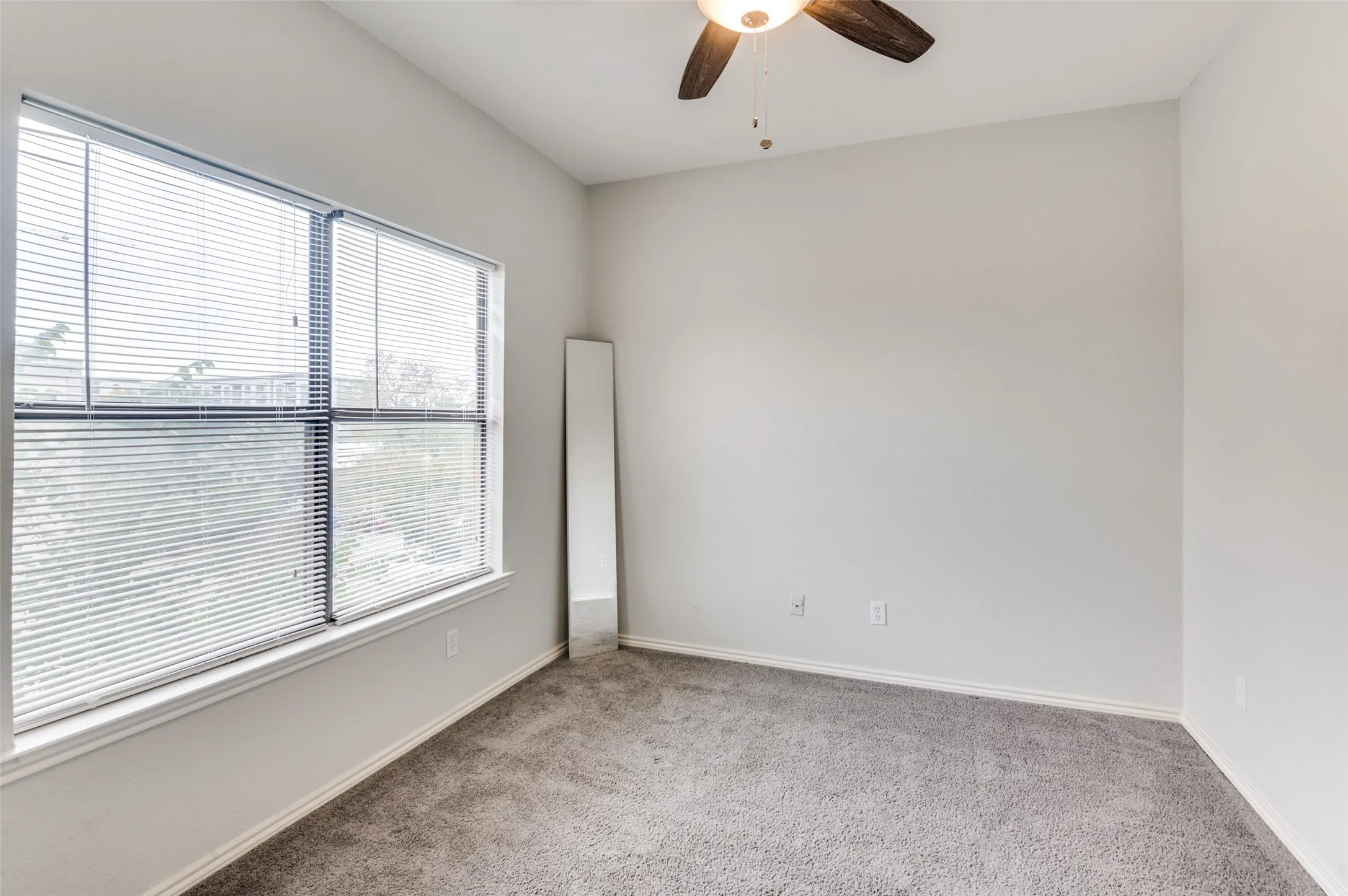 Bright room featuring a large multi-pane window with horizontal blinds, neutral wall paint, and gray carpet