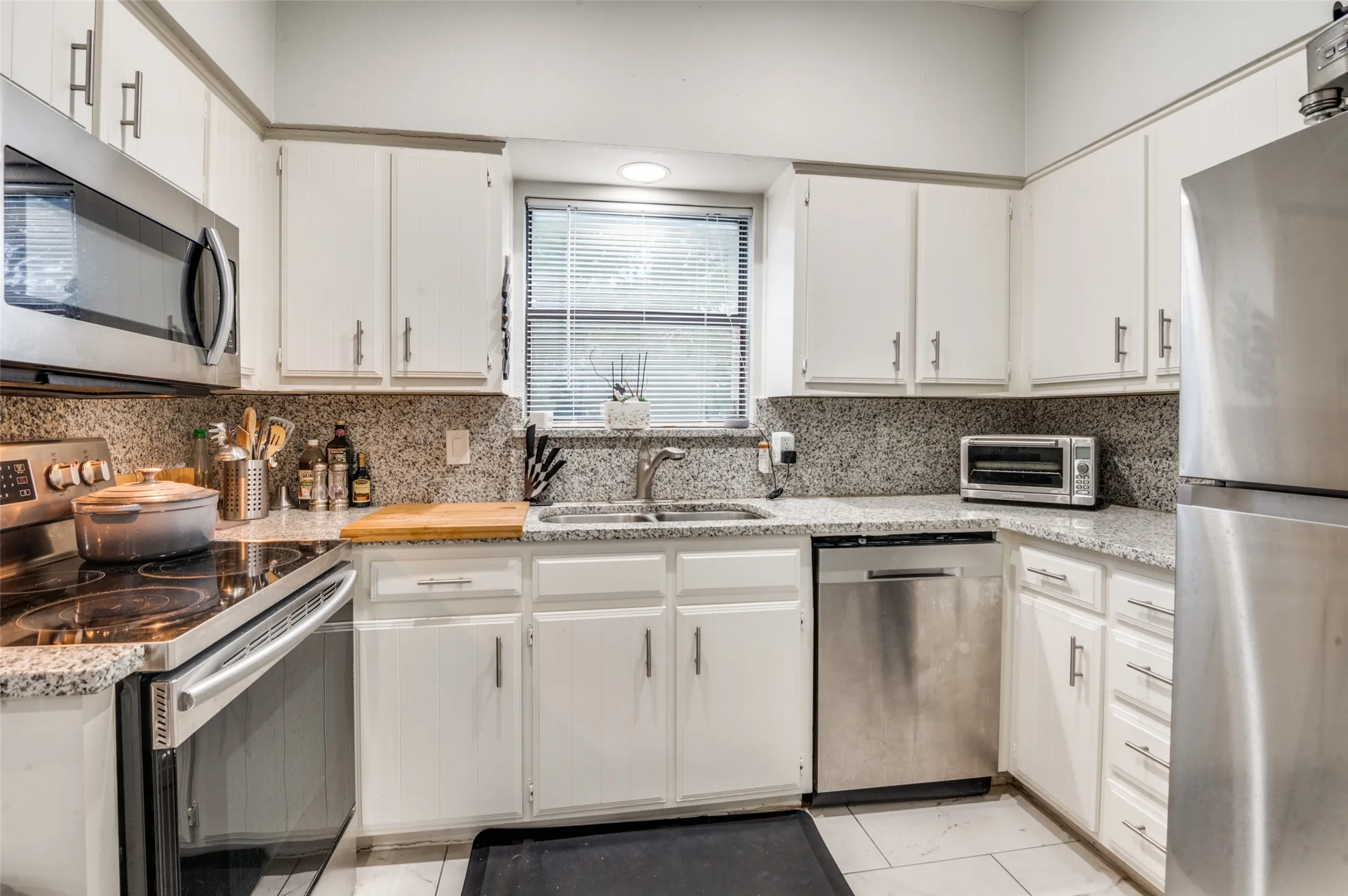Kitchen featuring white cabinetry, granite countertops, tile backsplash, and stainless steel appliances including a refrigerator, microwave, dishwasher, and electric range