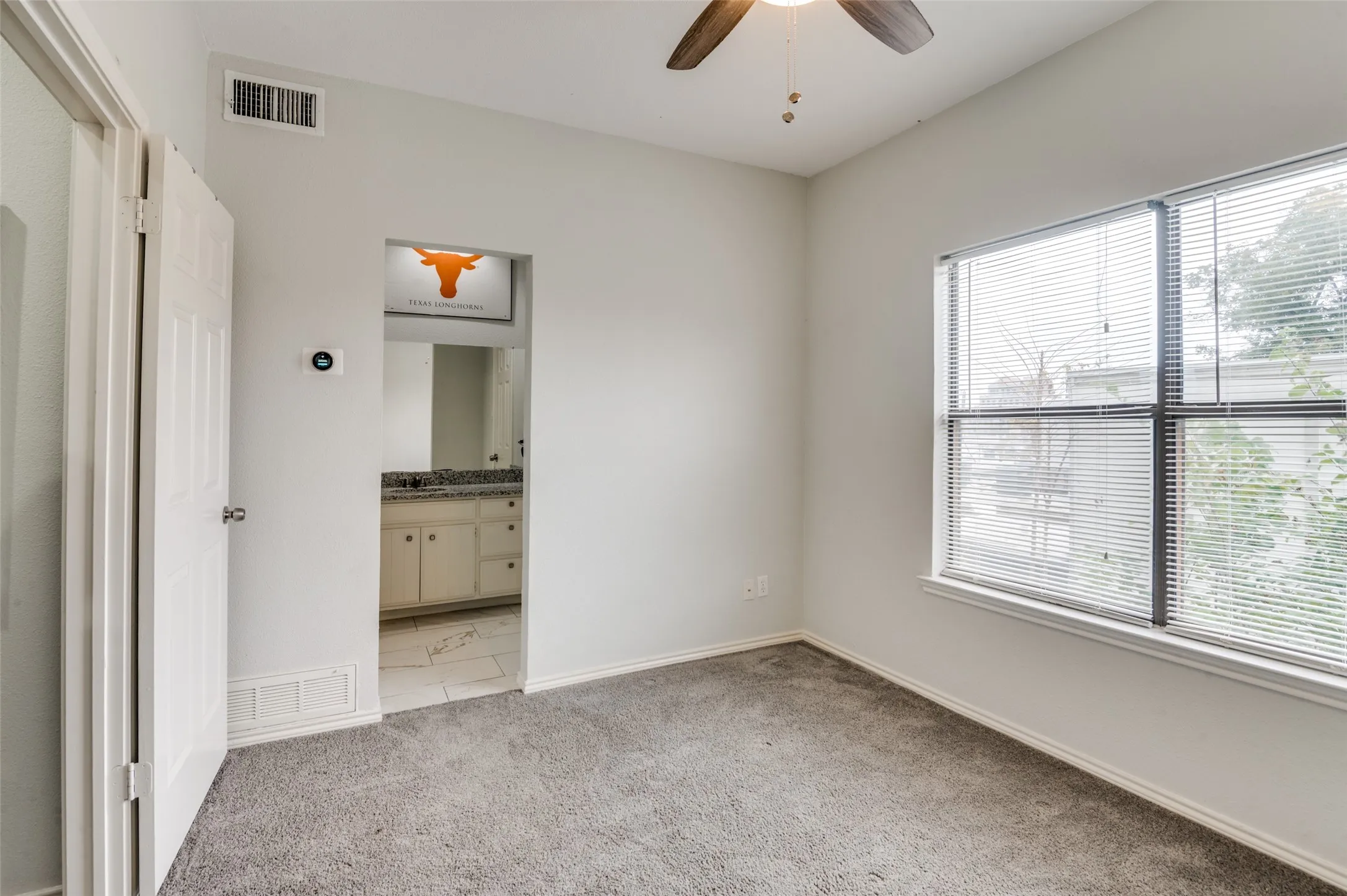 Carpeted room with a large window and a ceiling fan