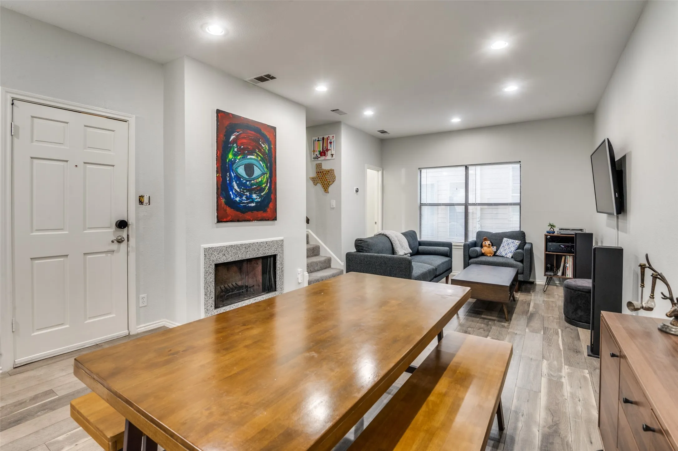 Open-concept living area featuring wood-finish flooring, recessed lighting, and a fireplace with a stone surround