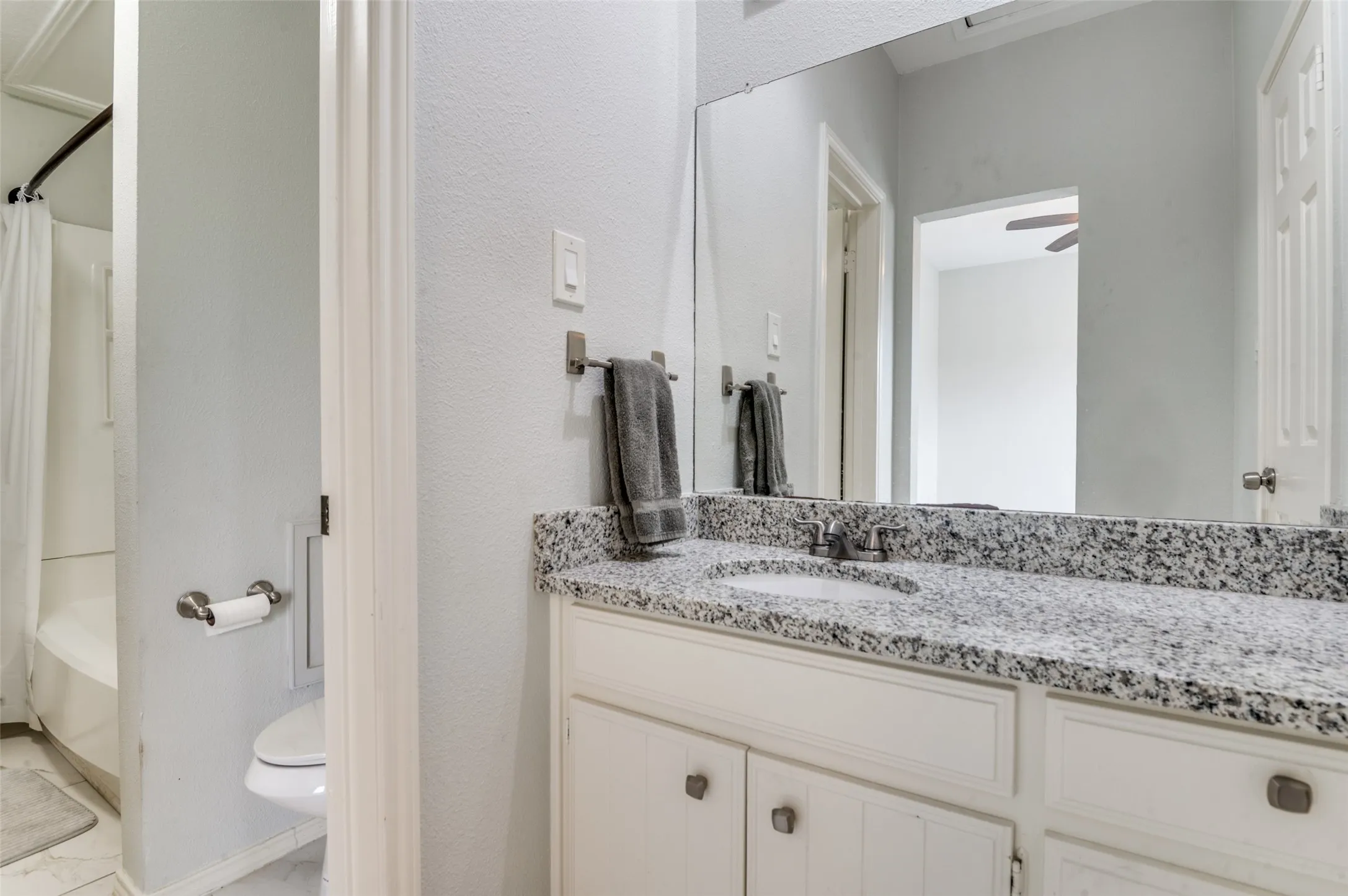 Bathroom featuring a dual vanity with a speckled countertop, white cabinetry, undermount sinks, and an expansive wall-mounted mirror