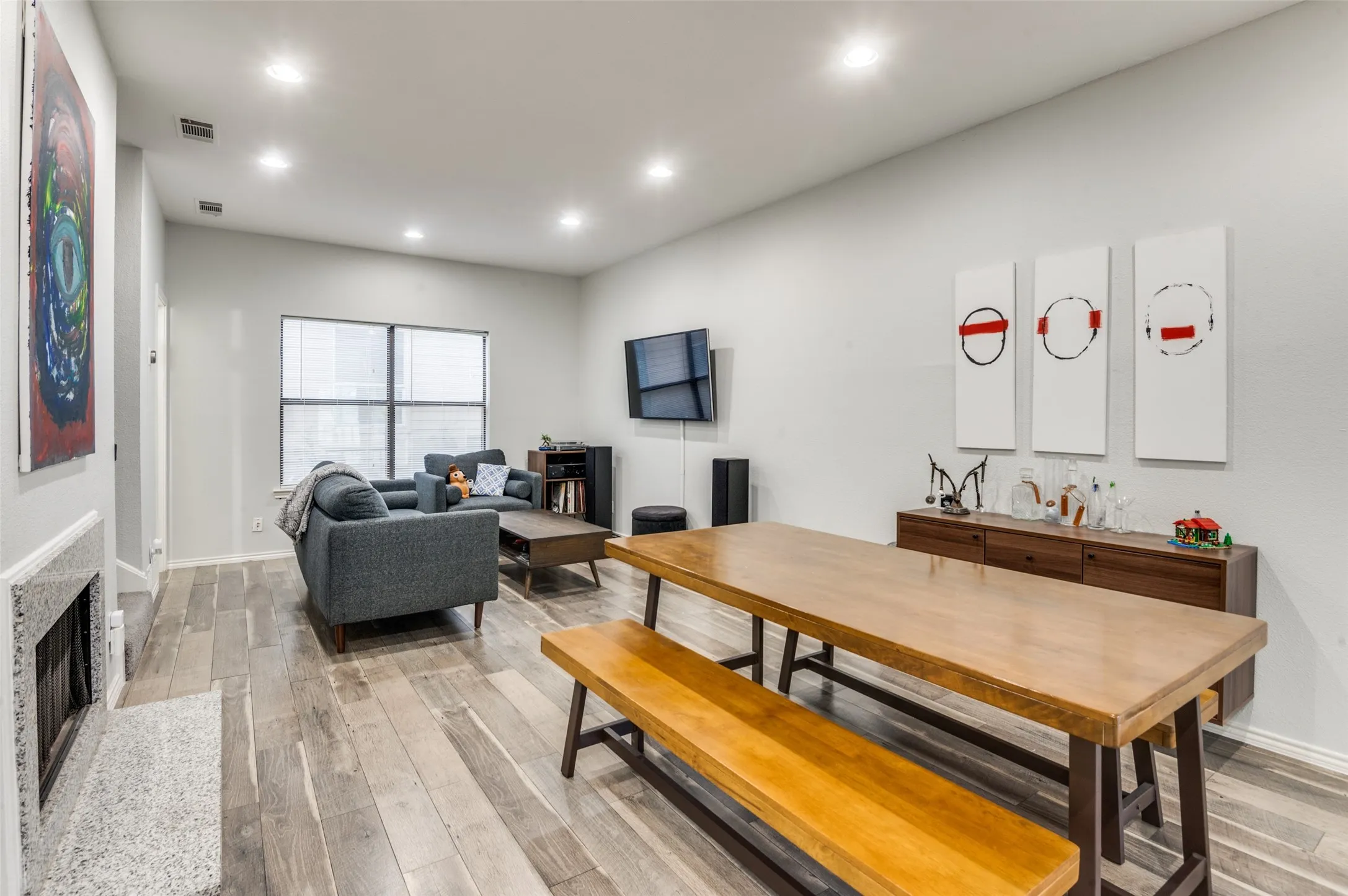 Open-concept living space featuring wood-finish flooring, recessed lighting, a stone-surround fireplace, and large windows