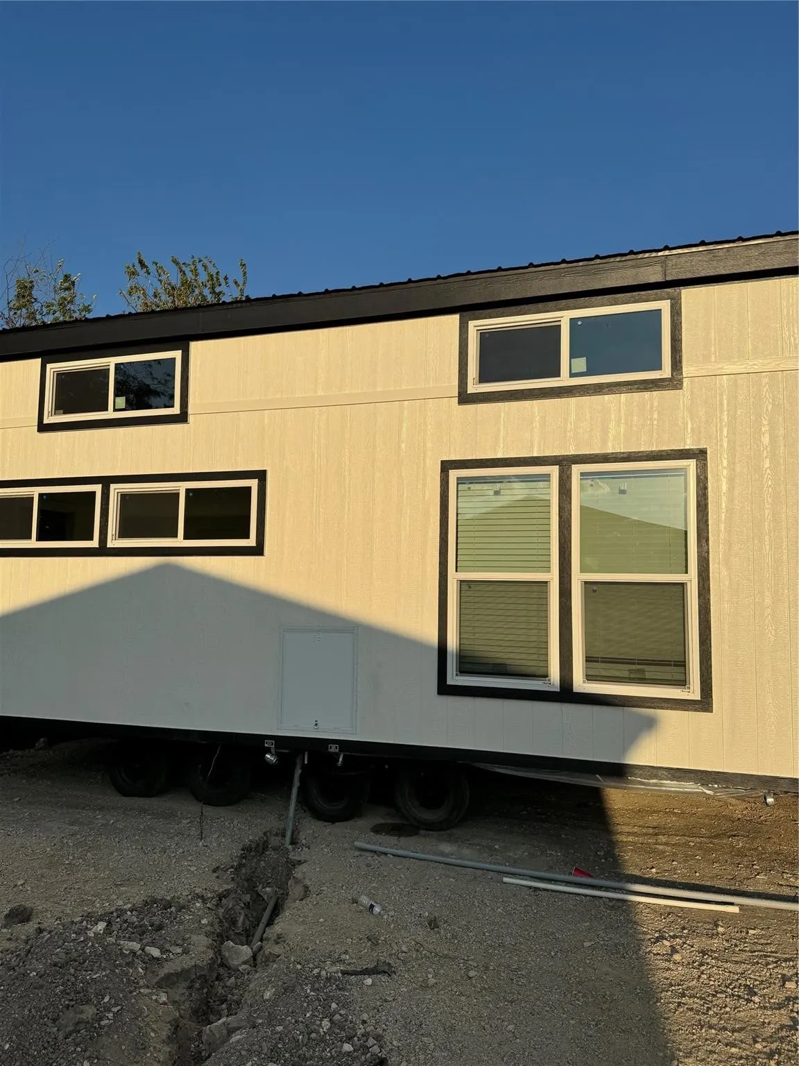 White vertical panel siding with black trim windows, a black roofline, and a multi-axle trailer base