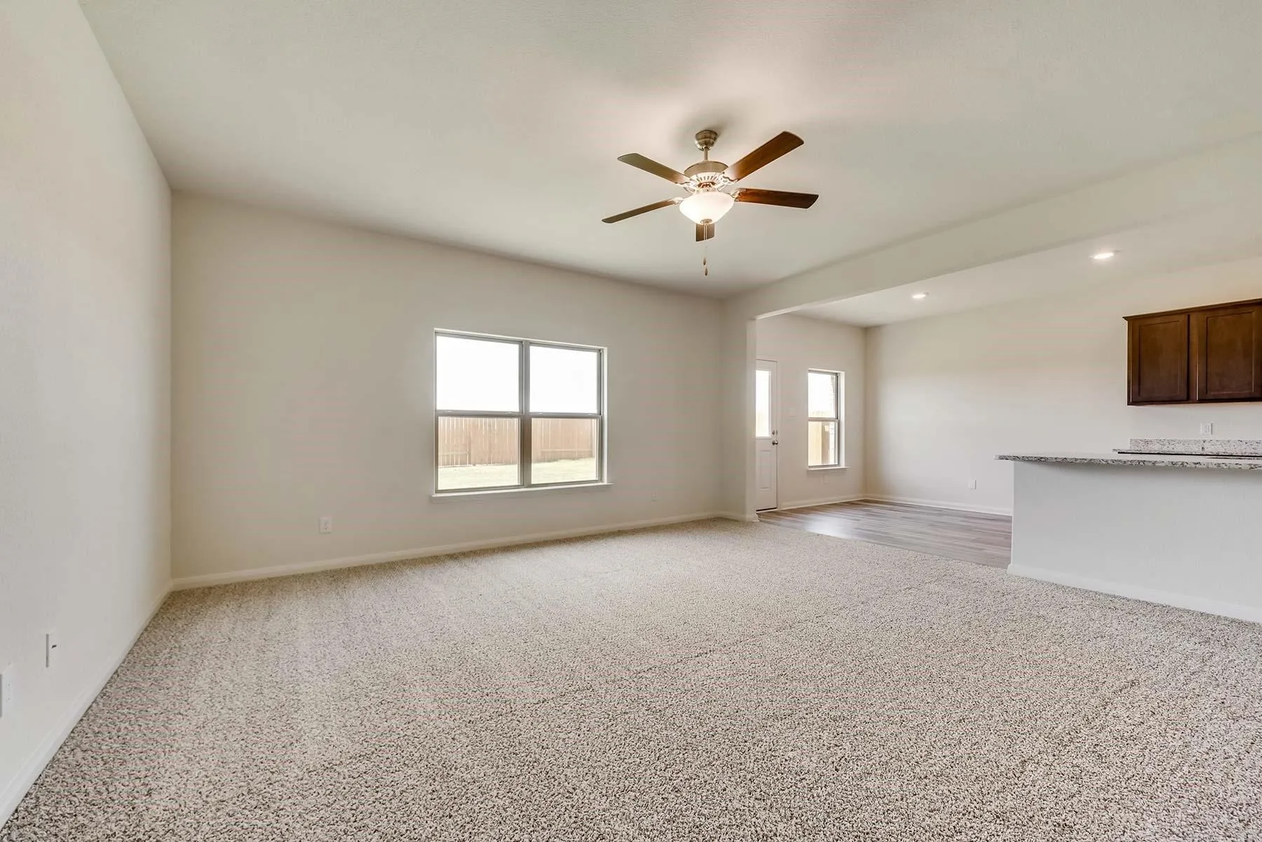 Spacious living area featuring neutral carpet and a ceiling fan with integrated lighting