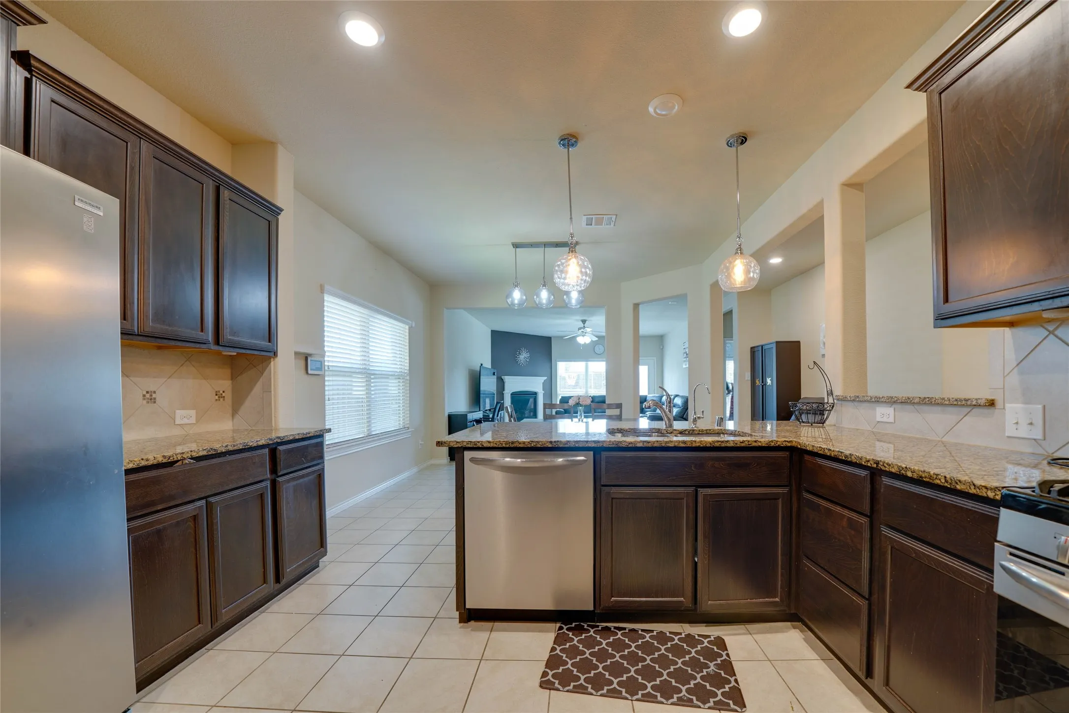 Kitchen featuring light tile patterned floors, kitchen peninsula, stainless steel appliances, decorative backsplash, and pendant lighting