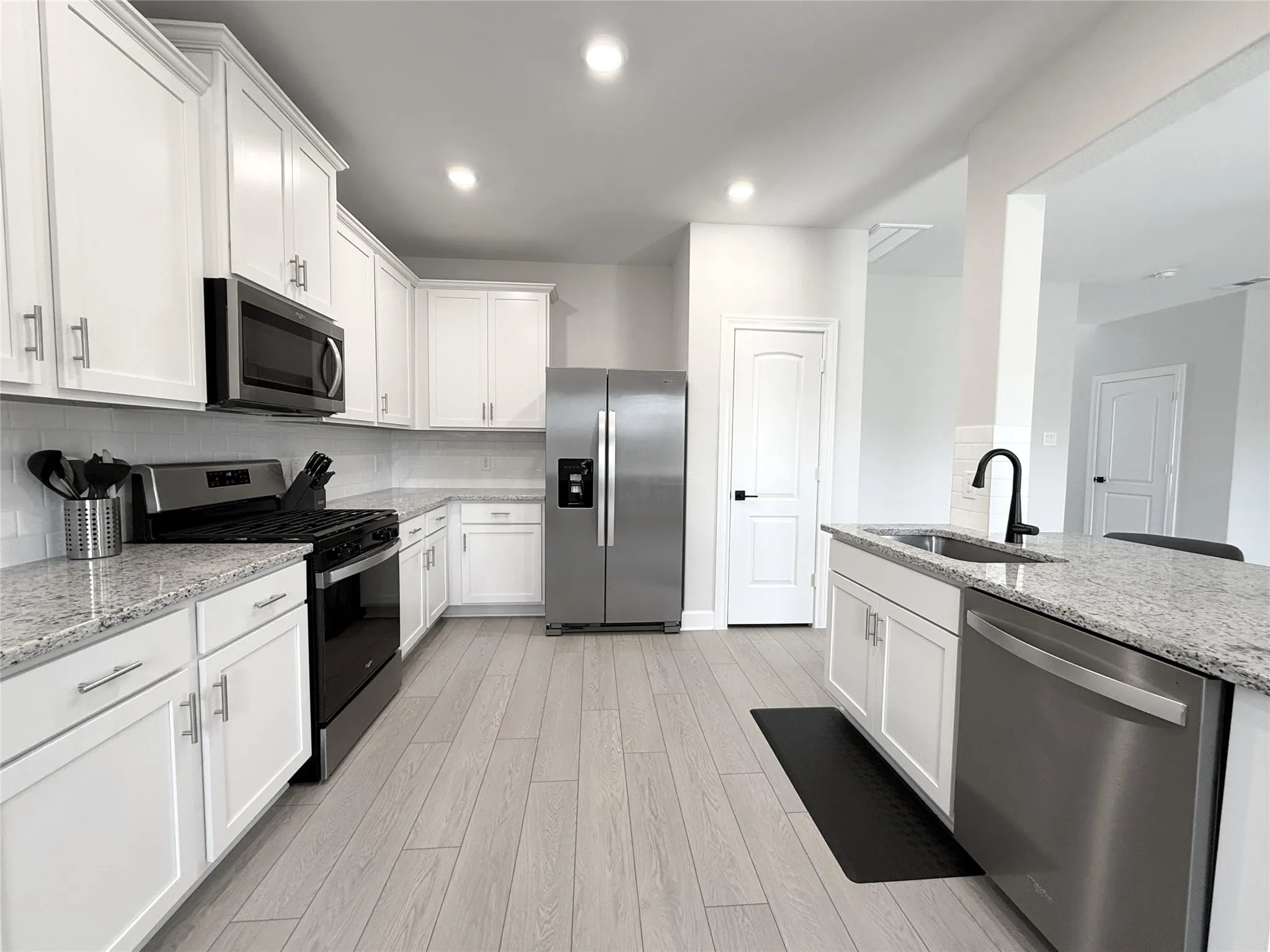 Modern kitchen featuring white shaker cabinetry, stainless steel appliances, light granite countertops, a subway tile backsplash, and wood-finish flooring