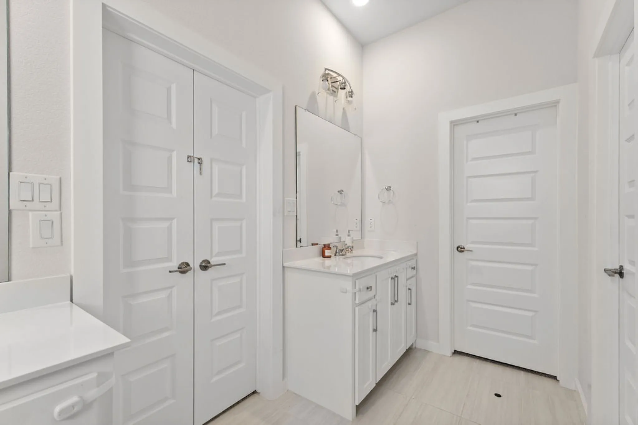 White bathroom vanity with a single basin sink, white countertop, and brushed nickel hardware