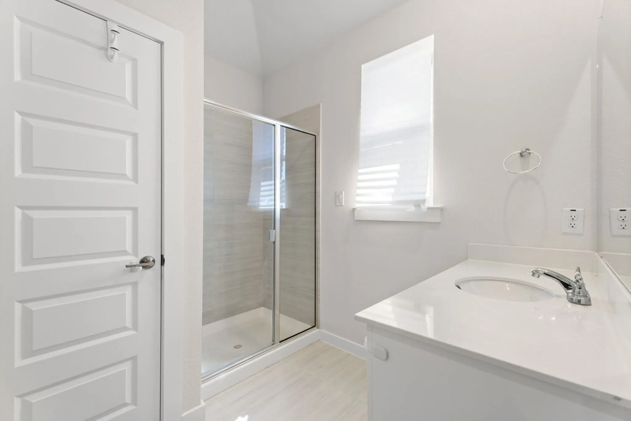 Bathroom featuring a glass-enclosed shower, white vanity with integrated sink, chrome faucet, white countertop, and contemporary window shade