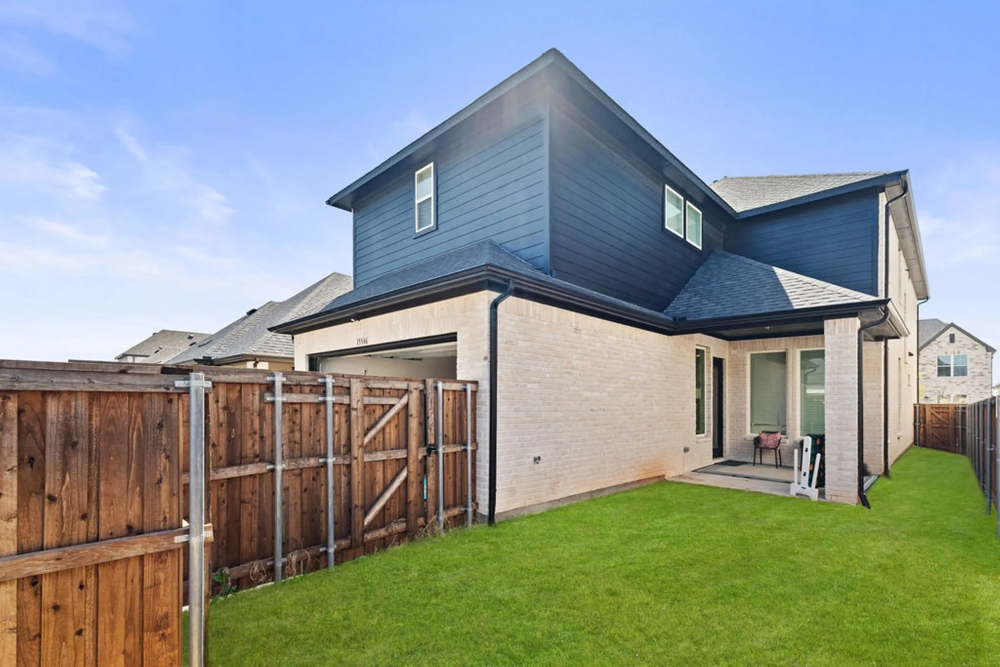 Rear exterior featuring light brick and dark siding, a covered patio, and a manicured lawn