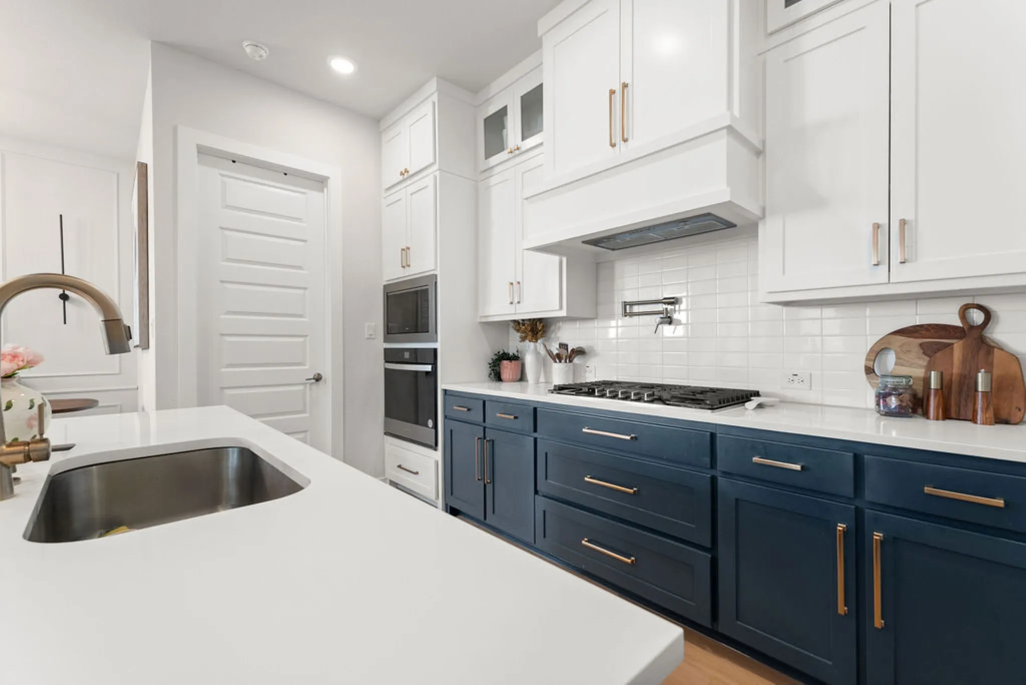 Kitchen featuring an island with an undermount sink, two-tone cabinetry with gold-tone hardware, white subway tile backsplash, and built-in appliances