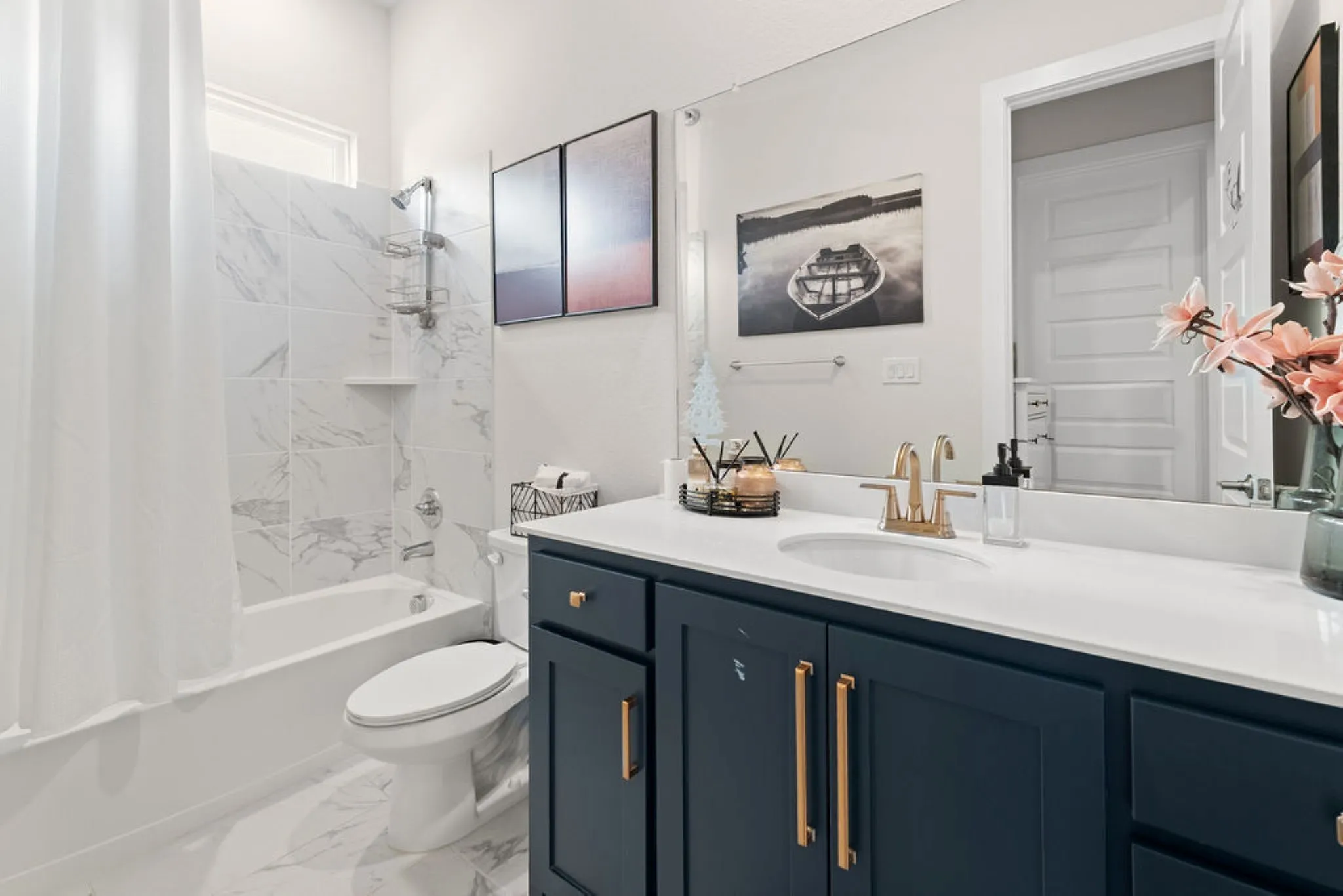 Bathroom featuring a white bathtub, white marble-patterned tile shower surround, and a dark blue vanity with gold-tone hardware