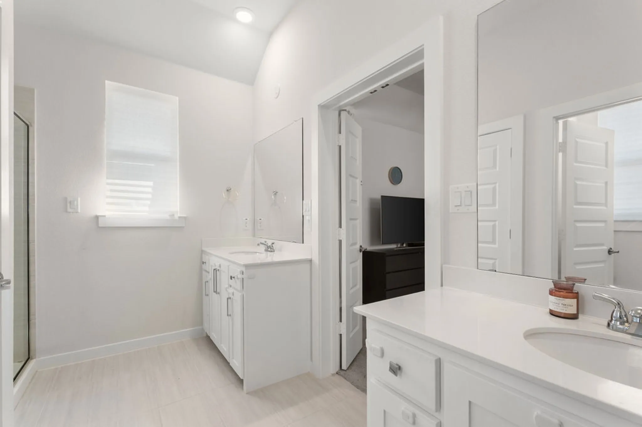 Bathroom featuring two single vanities with undermount sinks and light-toned countertops, a glass-enclosed shower, wood-finish flooring, and a window with blinds