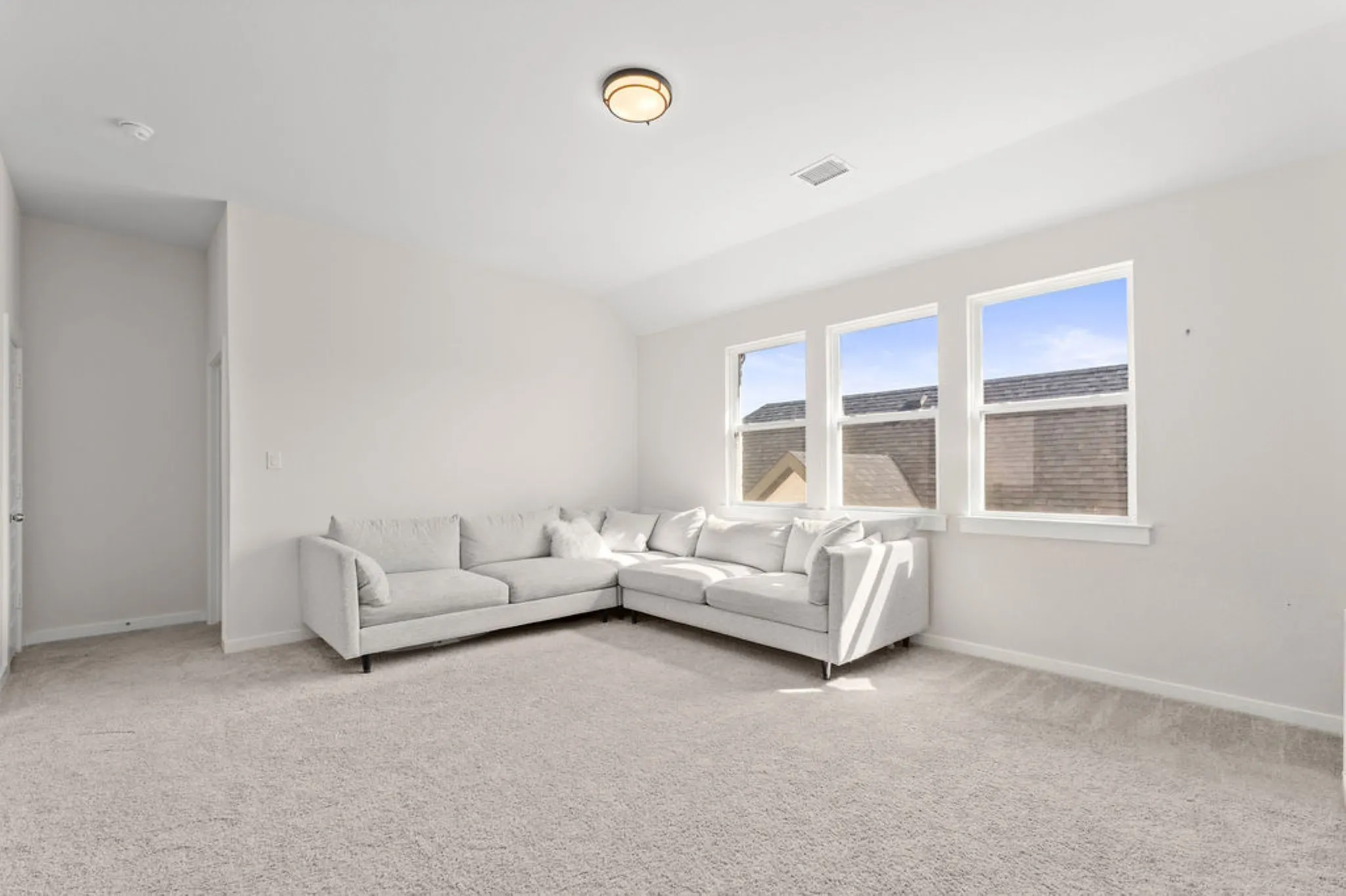 Spacious room featuring light-colored carpeting, three large windows, a flush-mount ceiling light fixture, and neutral wall tones