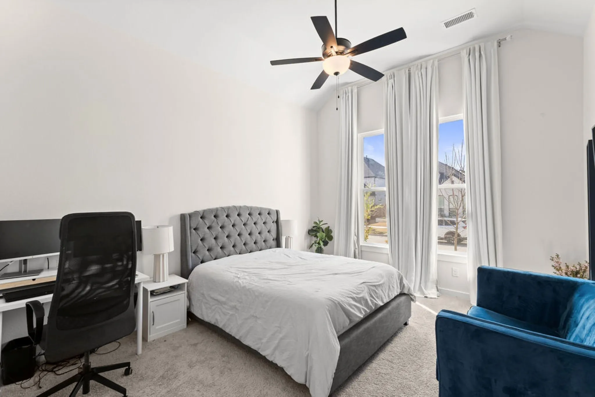 Vaulted ceiling bedroom featuring ample natural light from two tall windows, light neutral wall finishes, and soft carpet flooring
