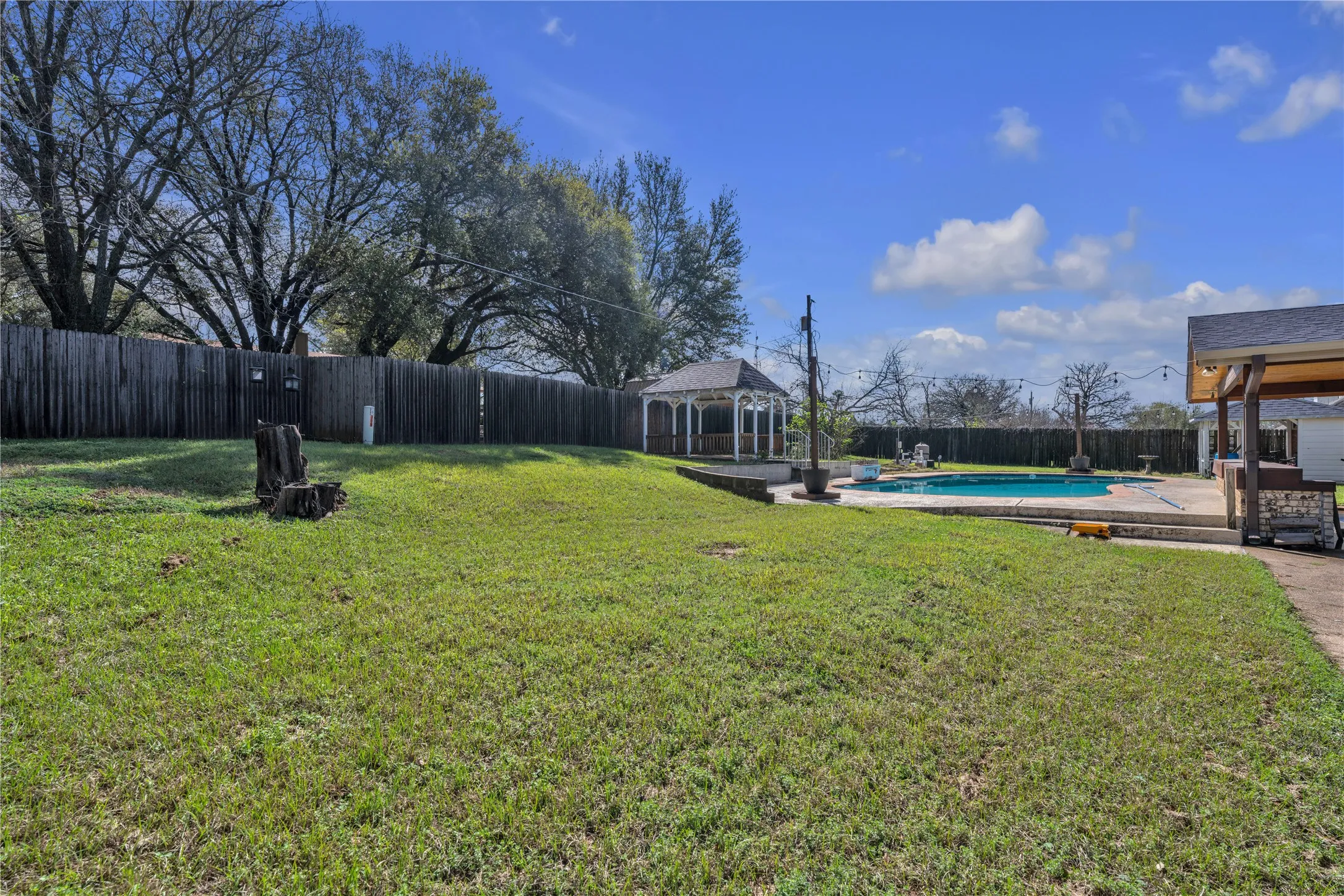 Expansive lawn area with a privacy fence, an in-ground swimming pool, a gazebo, and a covered patio structure