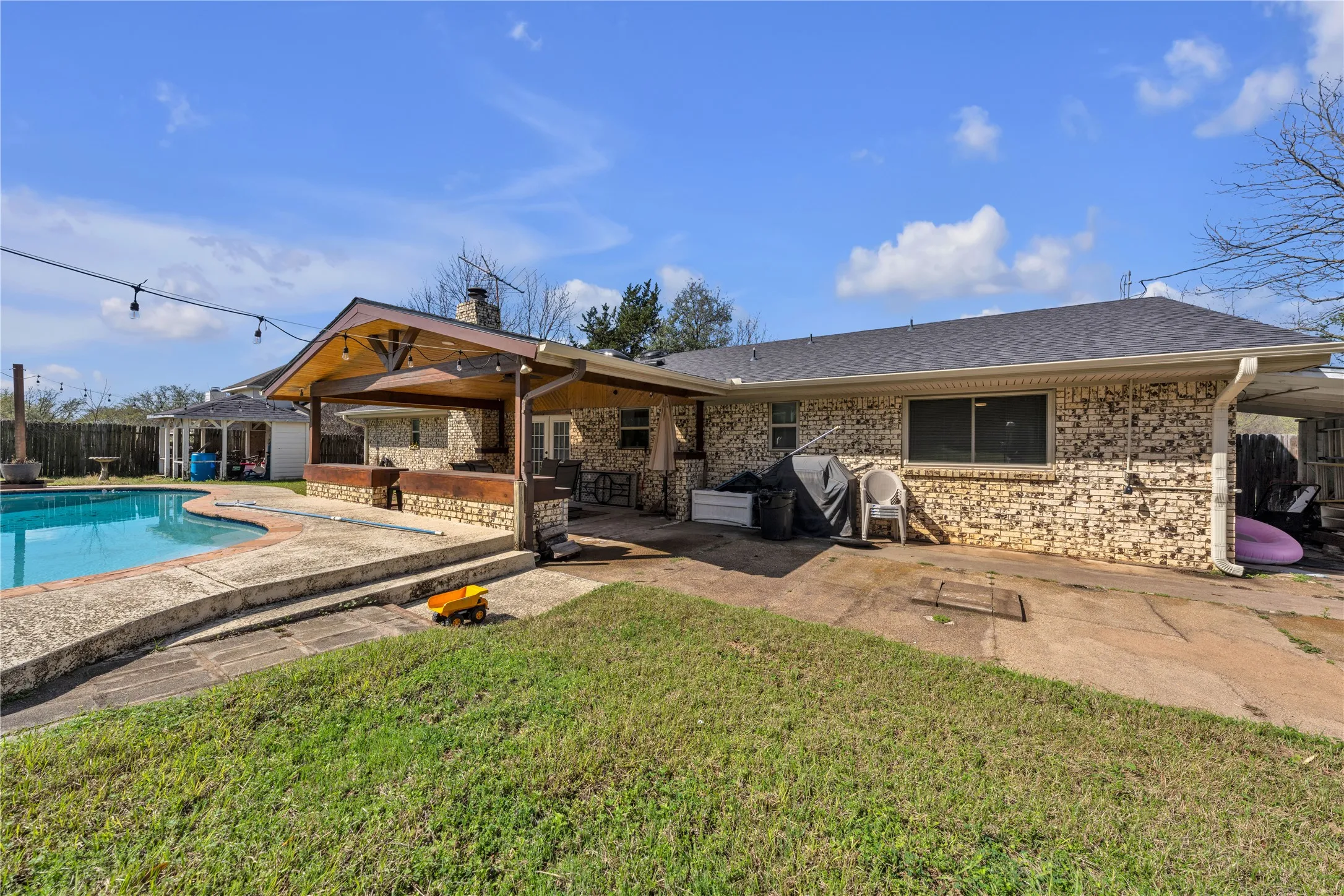 Outdoor entertaining area featuring a built-in stone bar with a wood-finish counter, covered patio with recessed lighting, and an in-ground swimming pool with a concrete surround