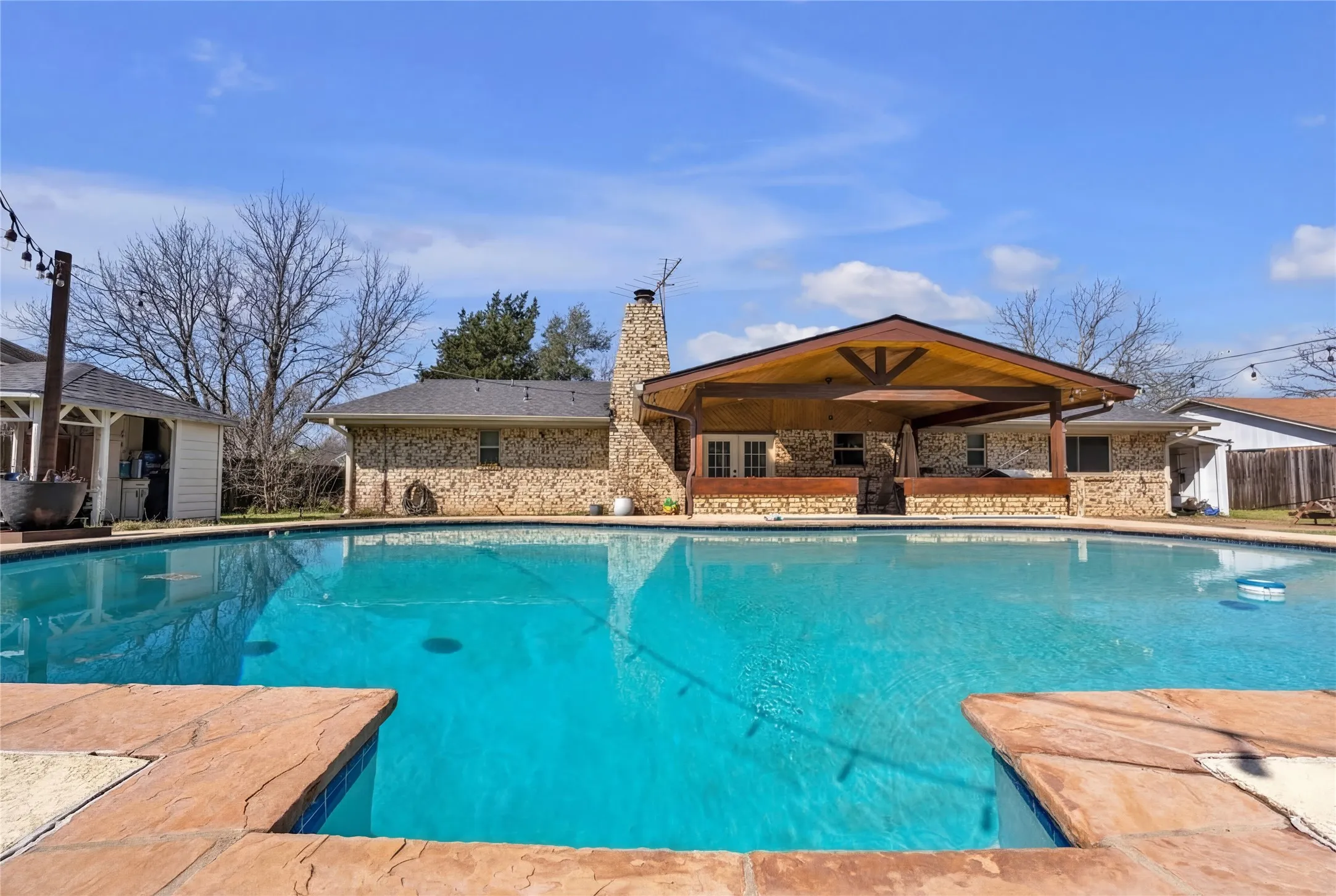 In-ground swimming pool with stamped concrete coping and a stone-clad outdoor living space