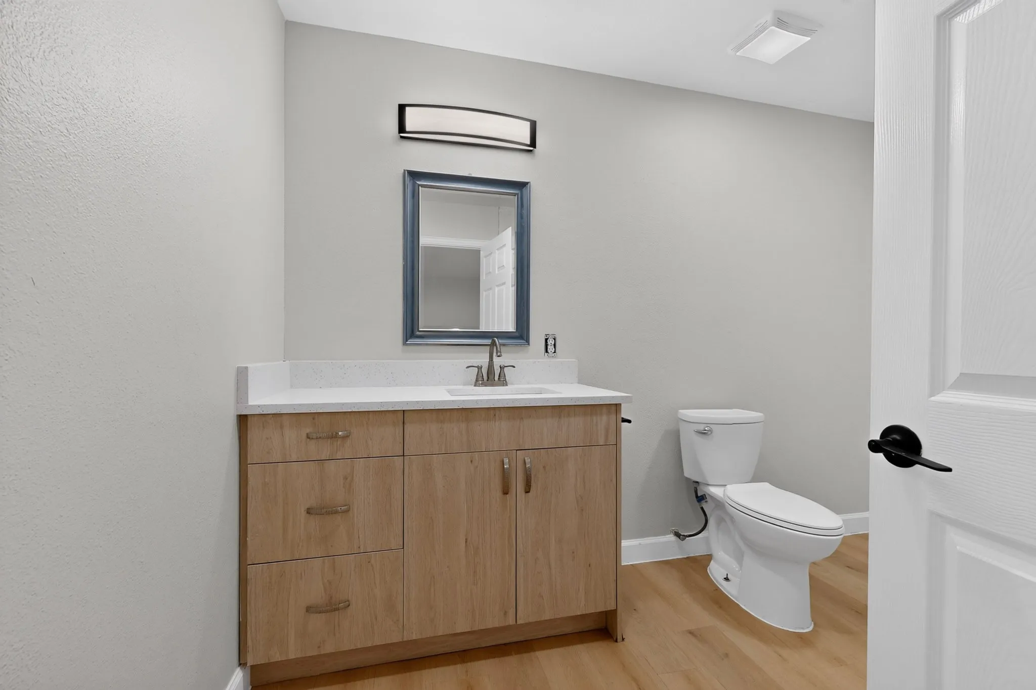 Bathroom featuring a wood-finish vanity with a light-toned countertop, a framed mirror, and a contemporary light fixture