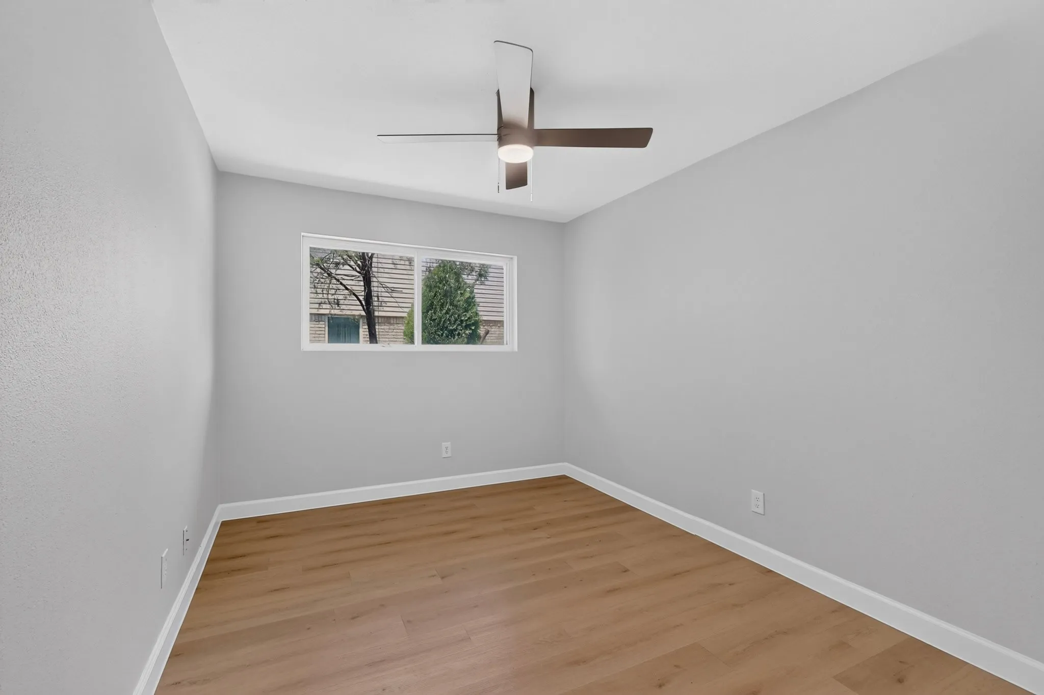 Interior space featuring wood-finish flooring, white baseboards, light gray walls, and a modern ceiling fan with integrated lighting