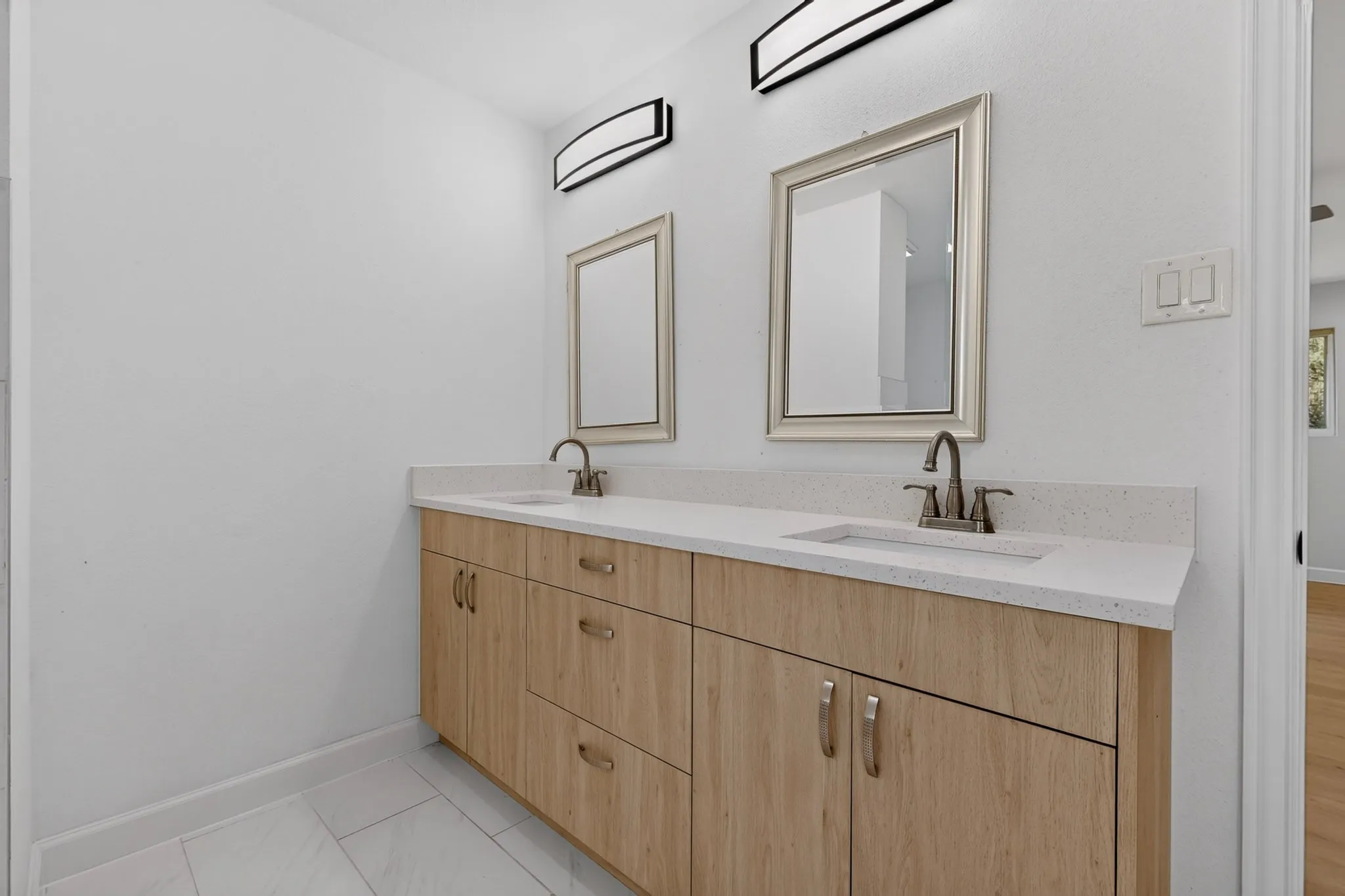 Dual vanity with light wood-finish cabinetry, white countertops, and integrated sinks