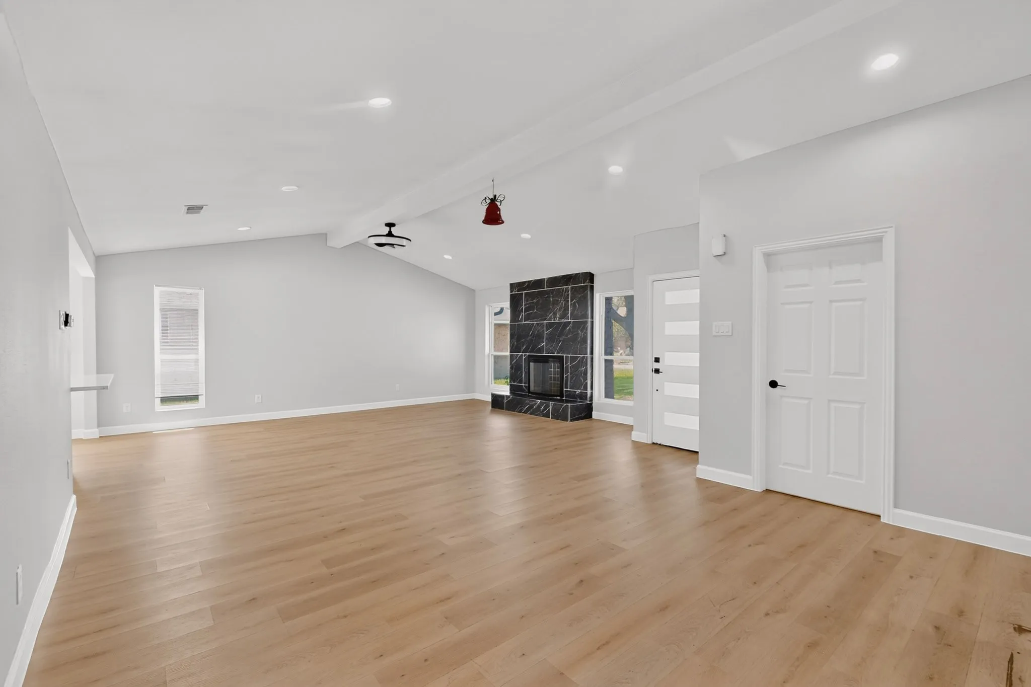 Spacious living area featuring wood-finish flooring, a vaulted ceiling with exposed beam, and recessed lighting