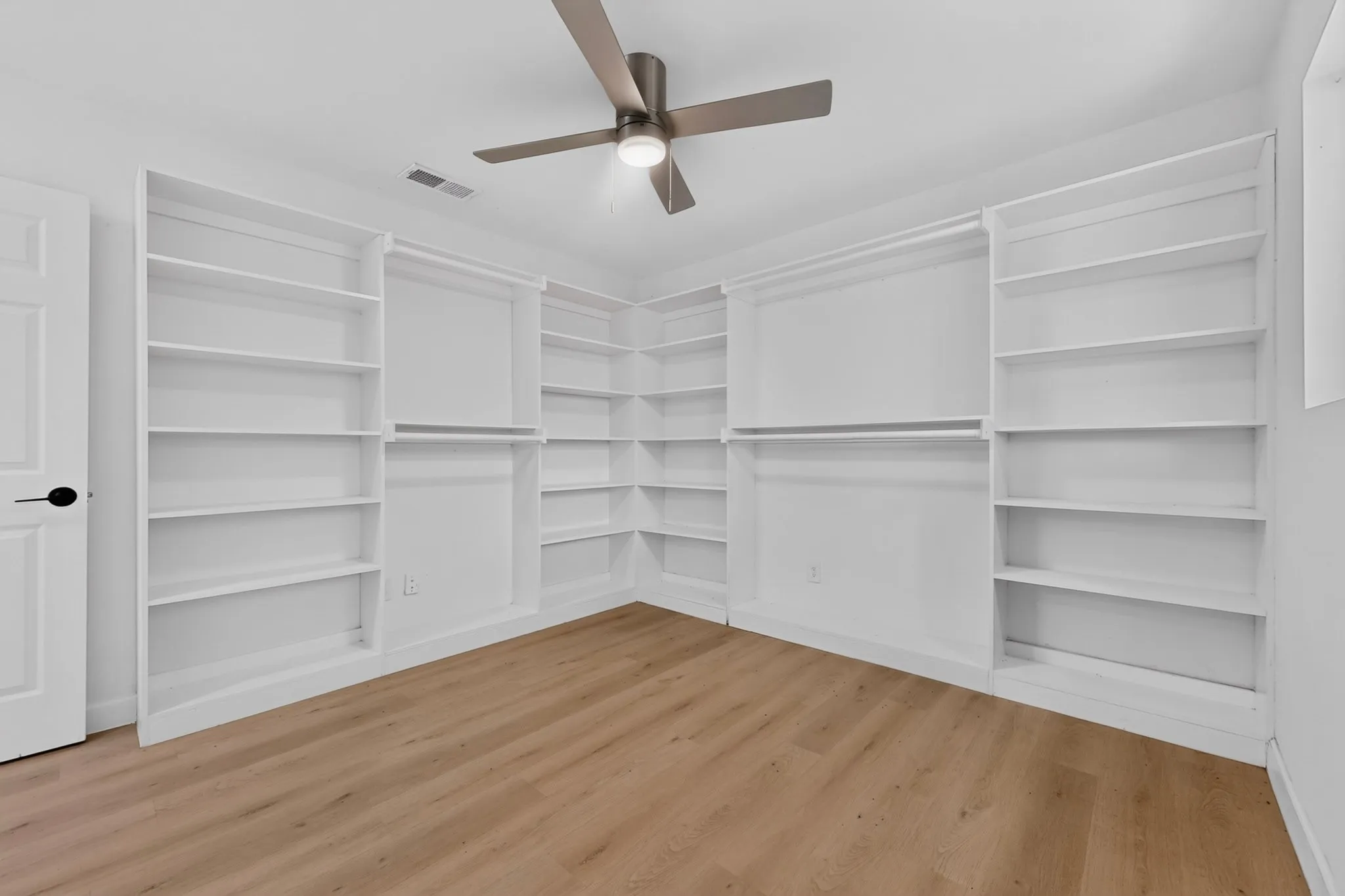 Room featuring extensive built-in shelving, hanging rods, and wood-finish flooring